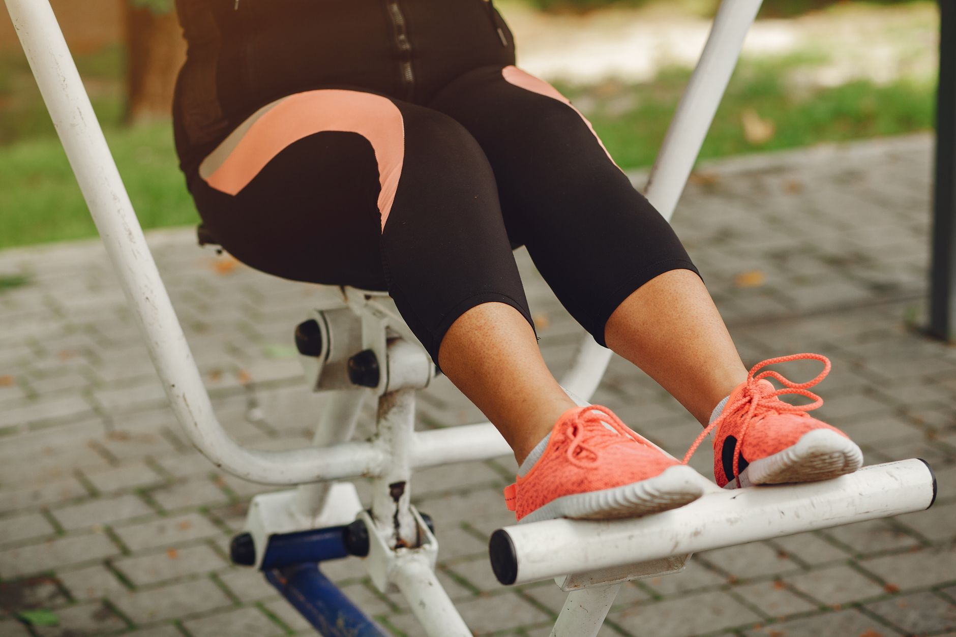 Close-up of a woman exercising on a fitness machine outdoors, focusing on her legs and shoes.