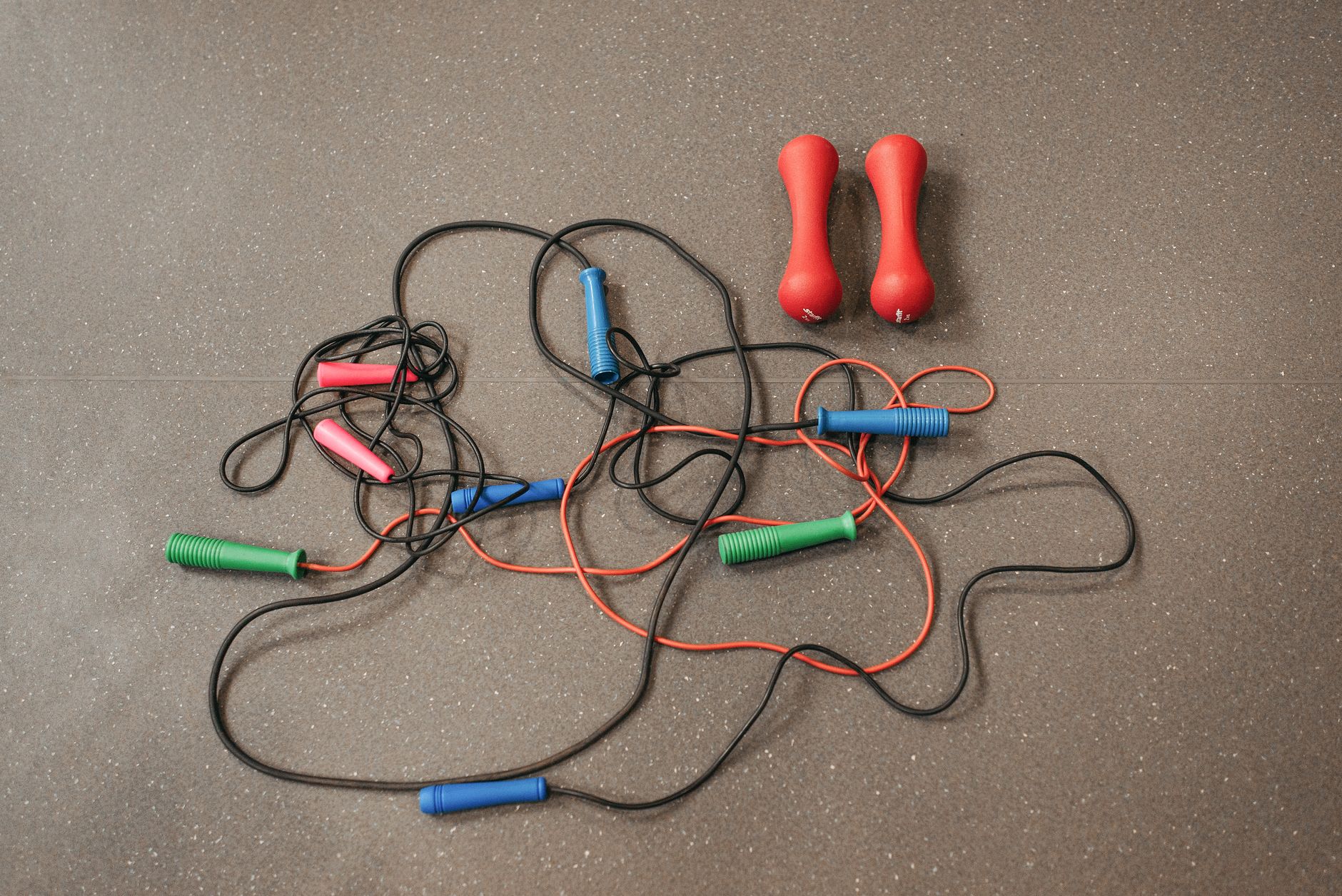 Vibrant jump ropes and dumbbells on a gym floor, perfect for home workouts.