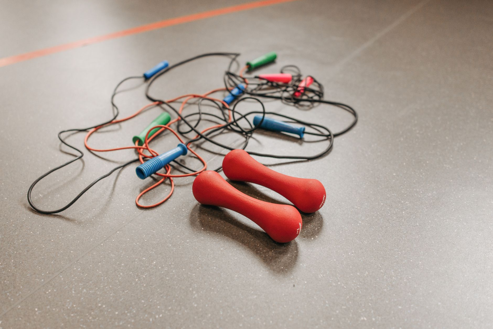 Tangled jump ropes and red dumbbells on a gym floor, highlighting fitness equipment essentials.
