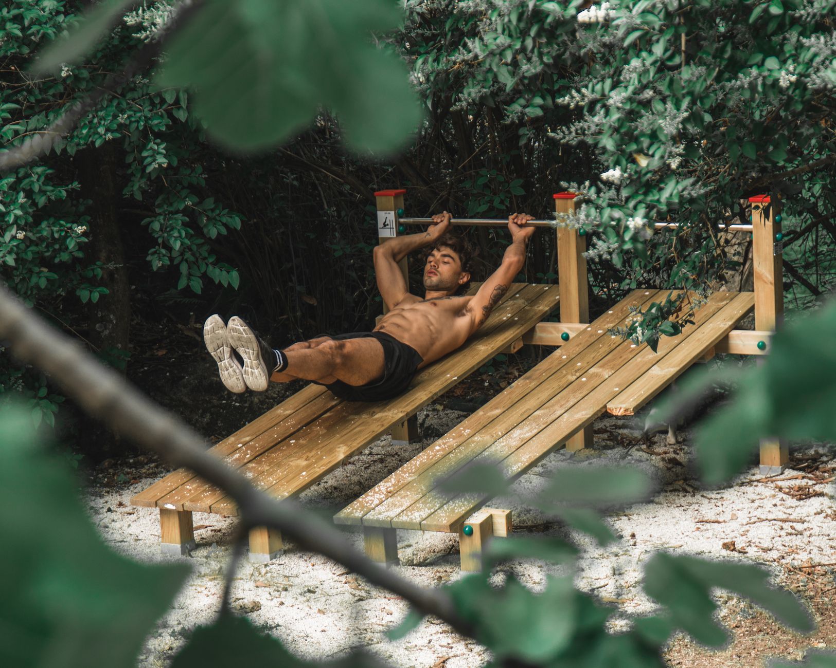 Asian man performing outdoor workout on wooden gym equipment surrounded by nature.