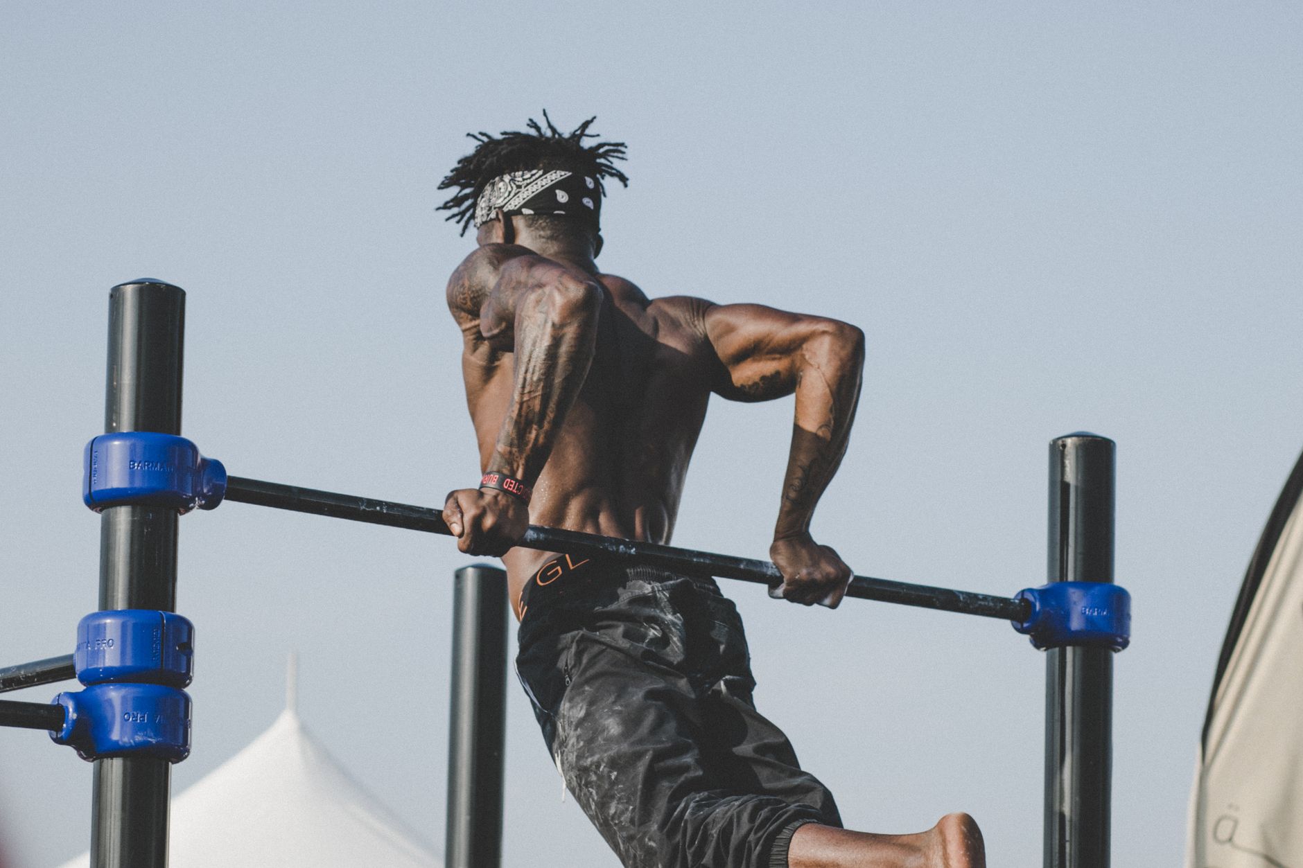 Muscular man exercising on a pull-up bar outdoors, showcasing strength and fitness.