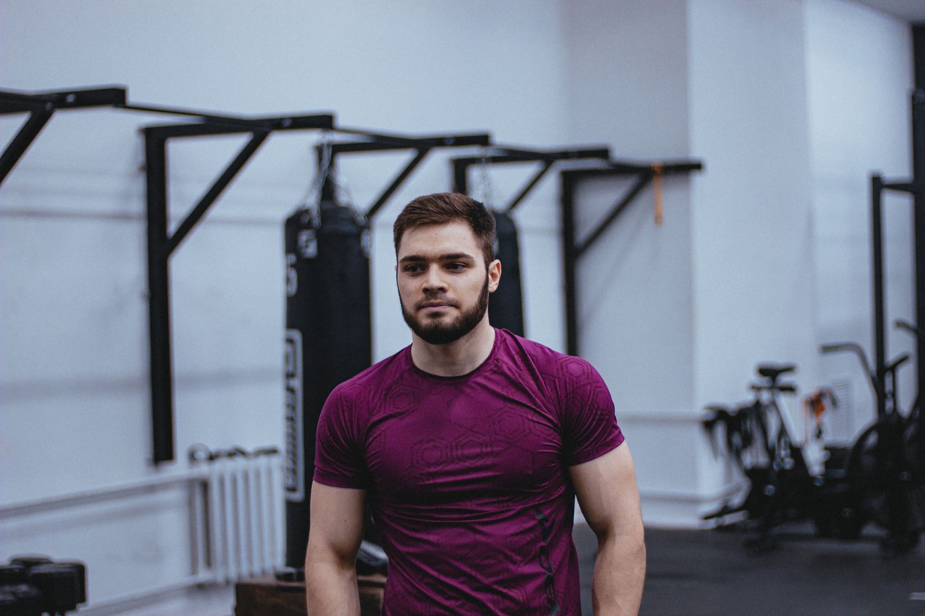 Caucasian man with beard working out in gym, wearing purple shirt, focused expression.