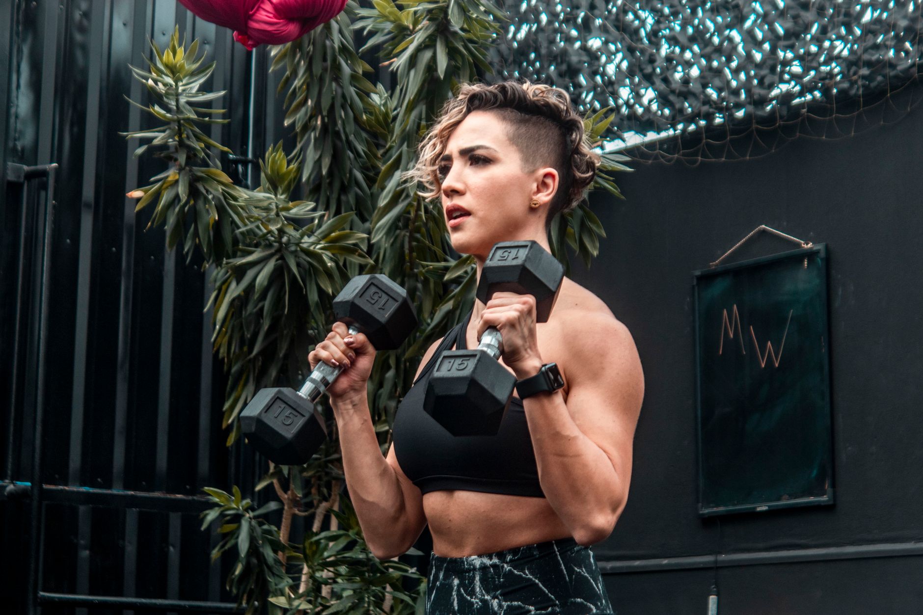 Confident woman exercising with dumbbells in an outdoor gym setting.