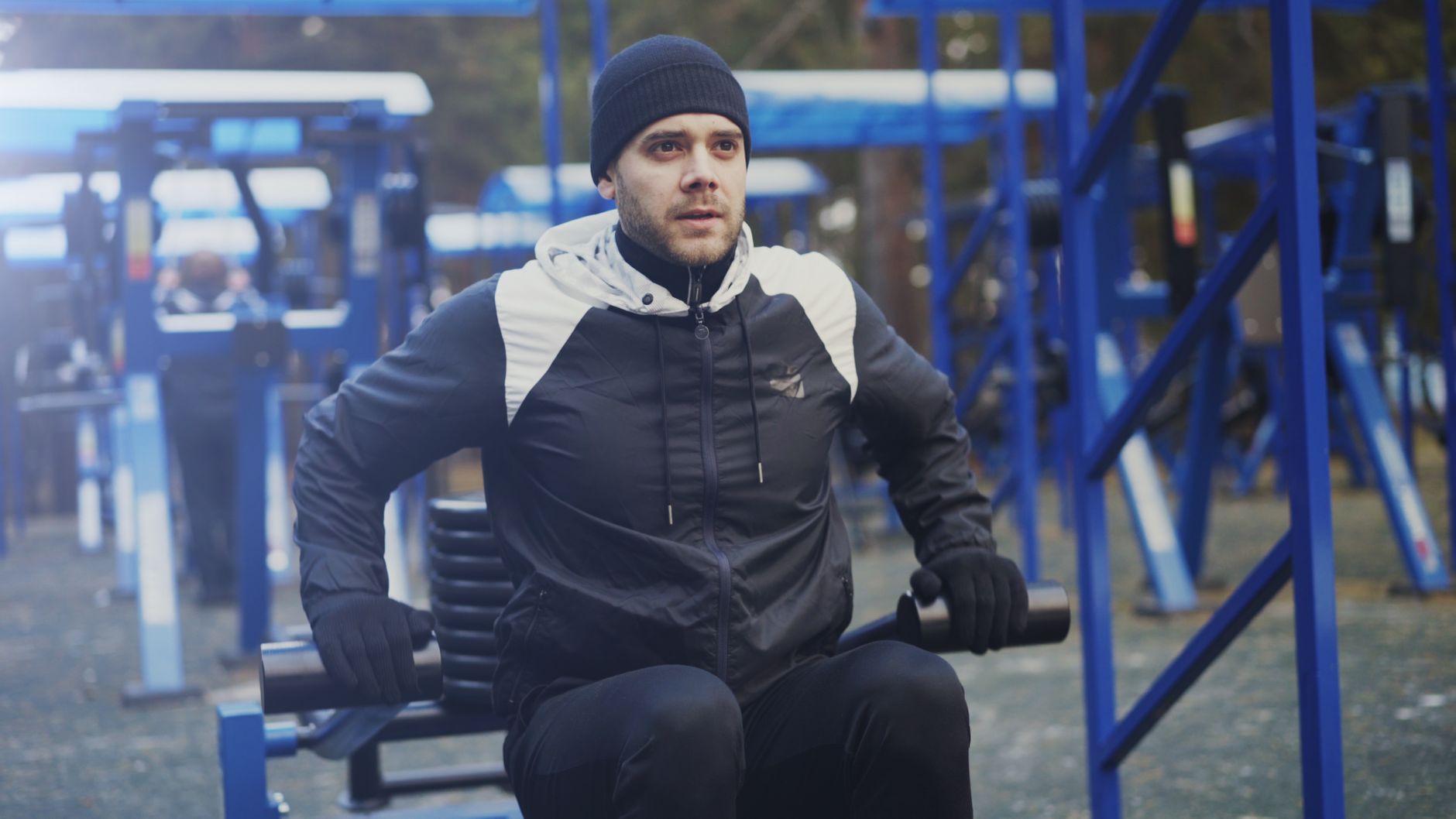 A man working out on outdoor gym equipment during a cool day, wearing winter clothes.