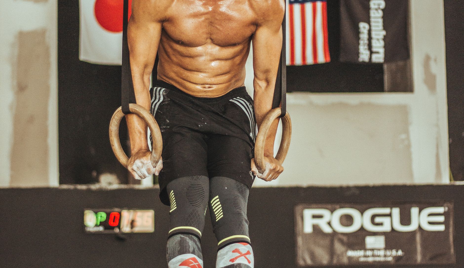 Strong athlete doing ring workout in a gym, showcasing muscular physique and strength training.