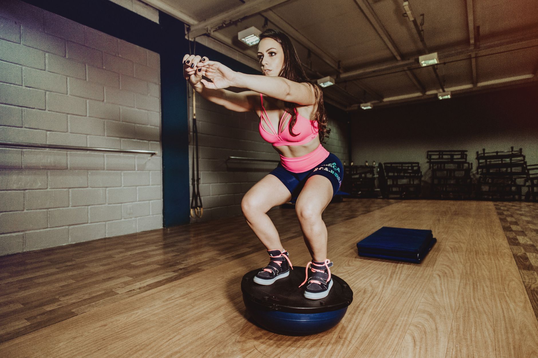 Full body concentrated fit sportswoman in sports bra and shorts performing squats while balancing on bosu ball during workout in modern fitness center