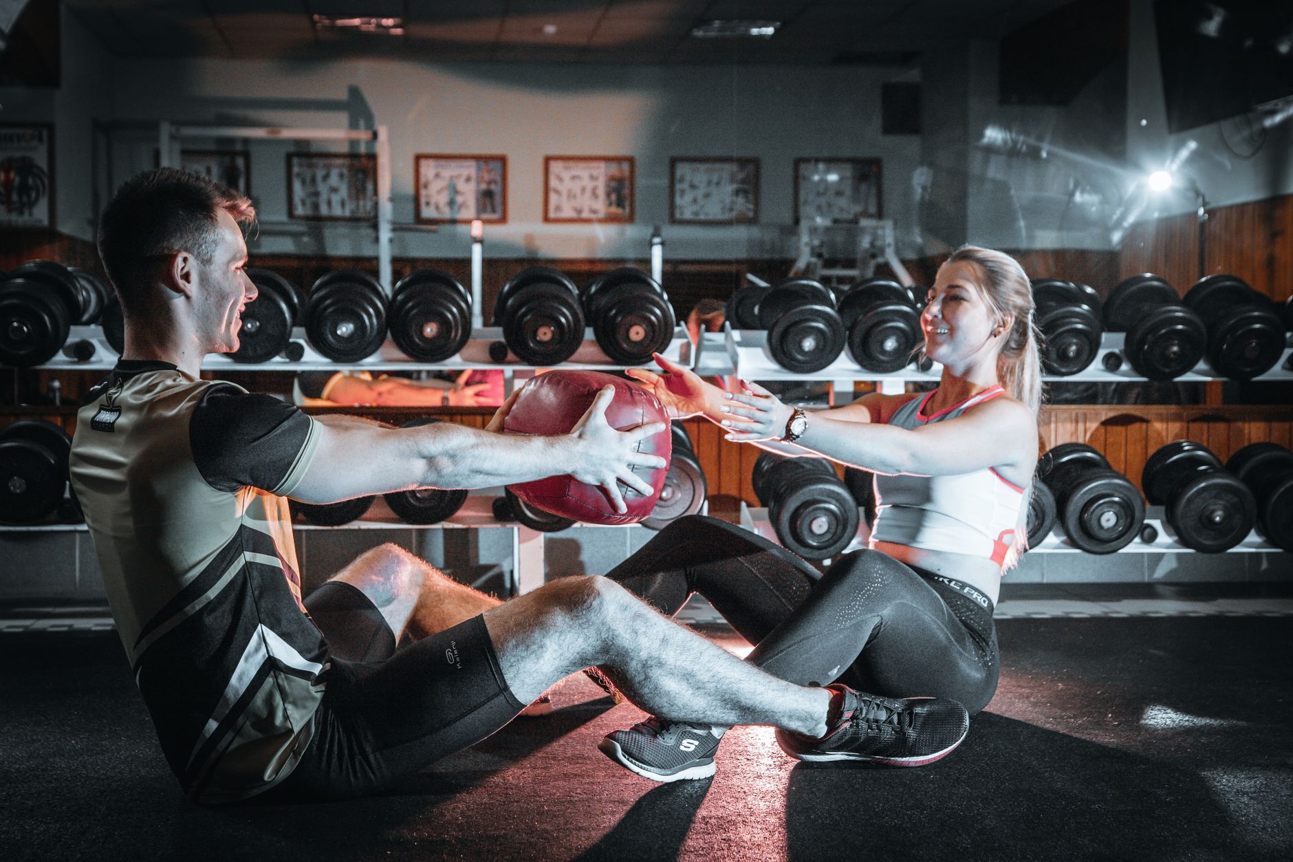 A couple engaged in a fitness session using a medicine ball in a gym environment.