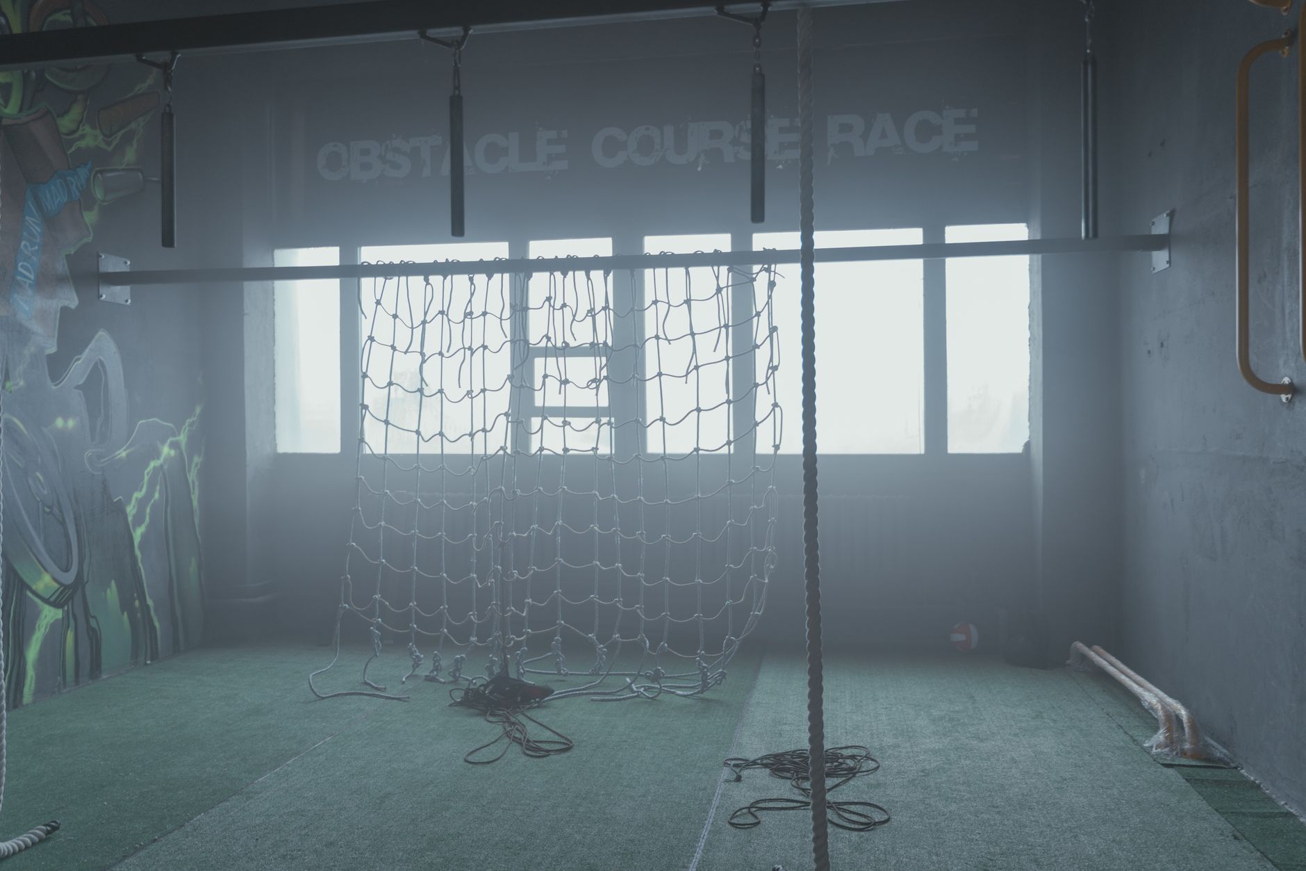 Indoor gym featuring a cargo net and ropes for obstacle course training.