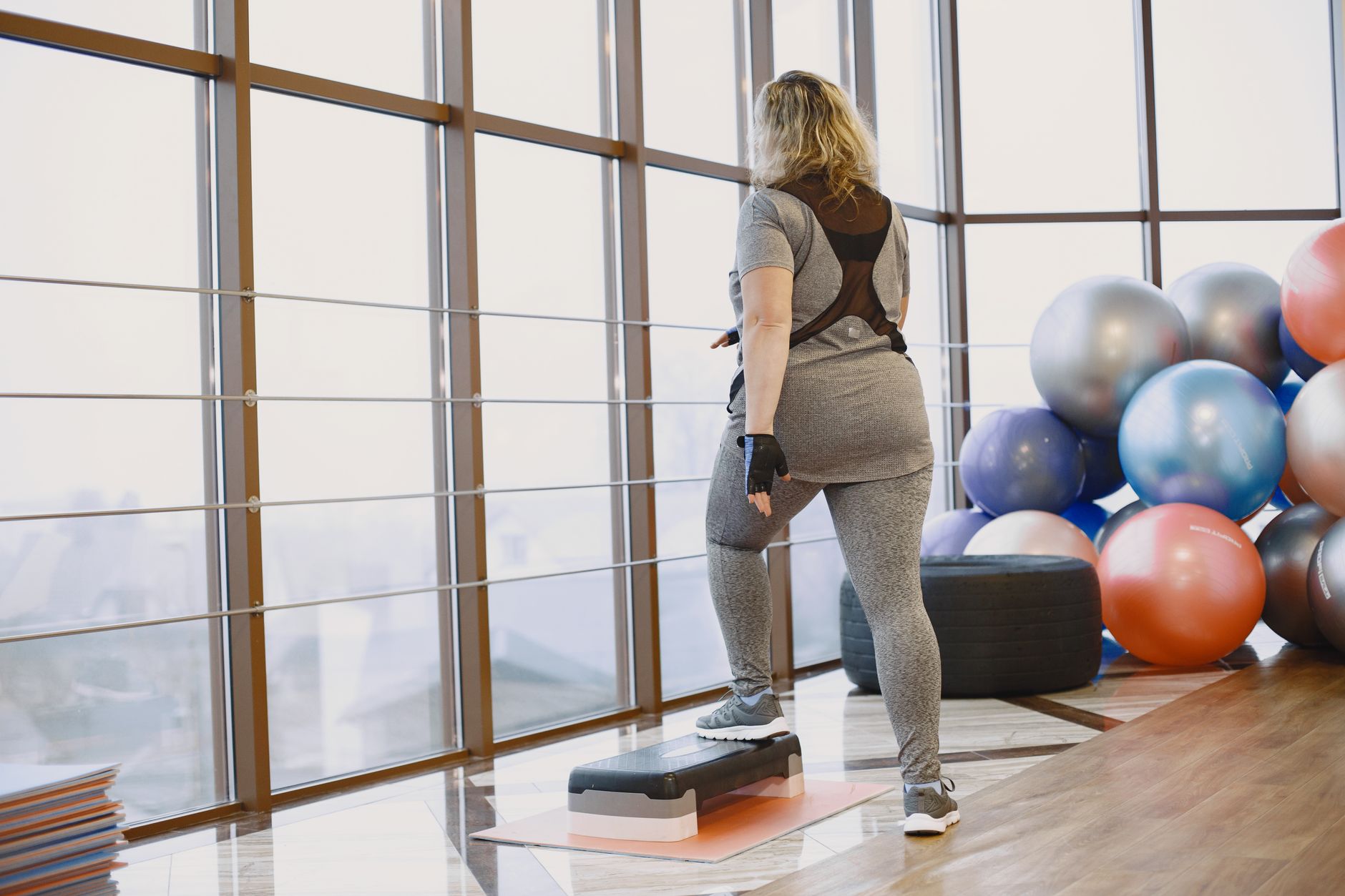 Back view of a woman exercising indoors with fitness equipment and step platform.