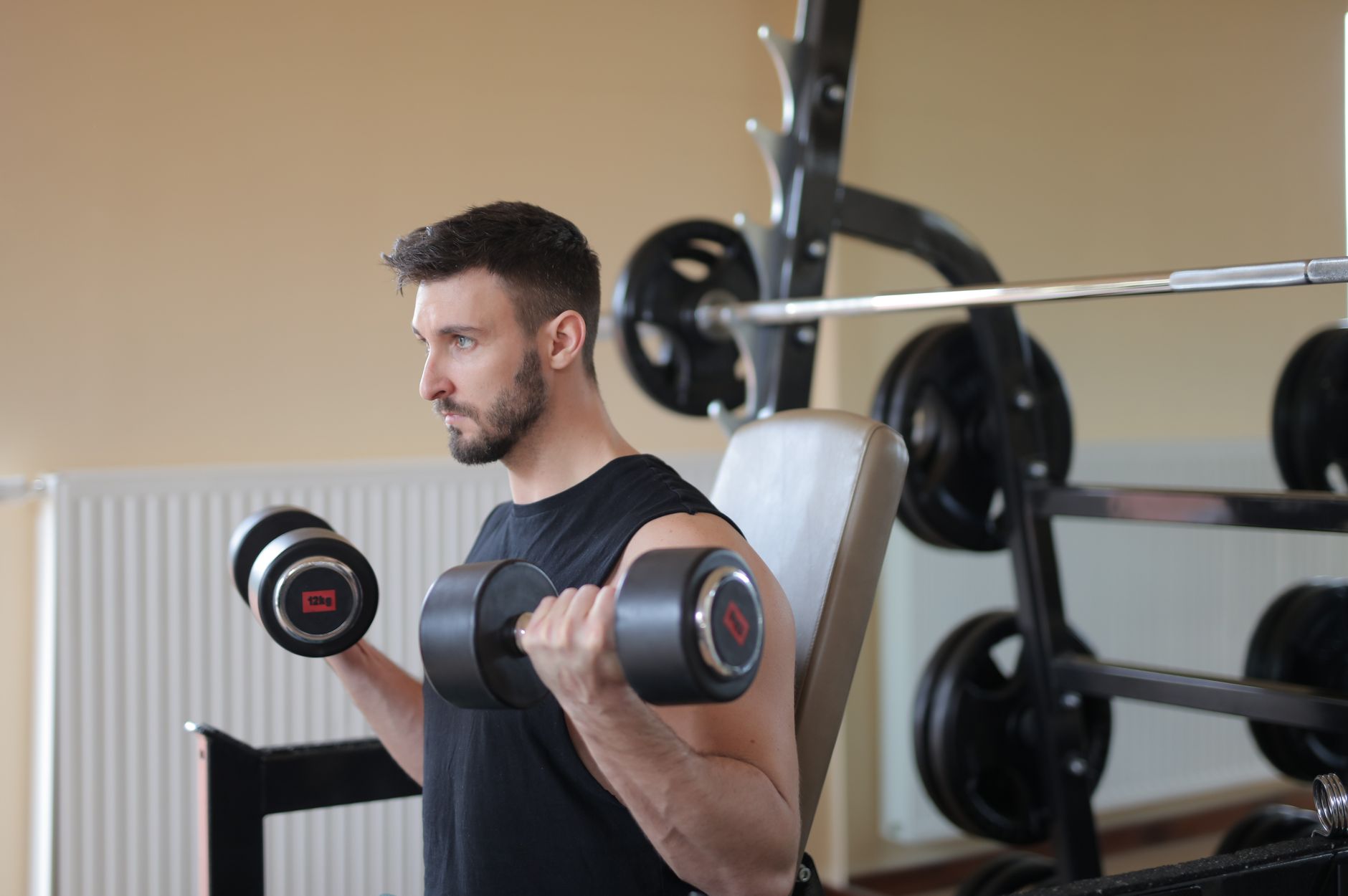Focused man lifting dumbbells for bicep curls in gym, emphasizing strength and fitness.