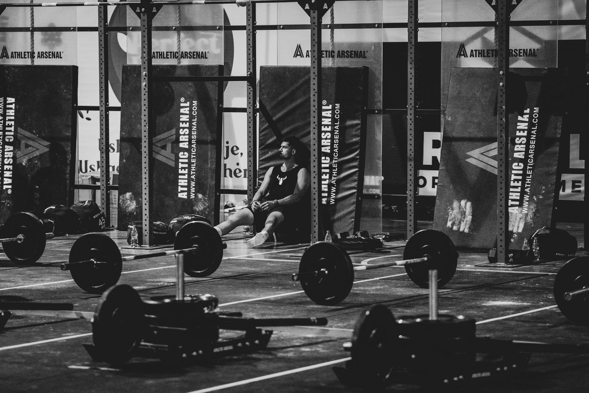 Black and white photo of a man resting in a gym surrounded by weights.