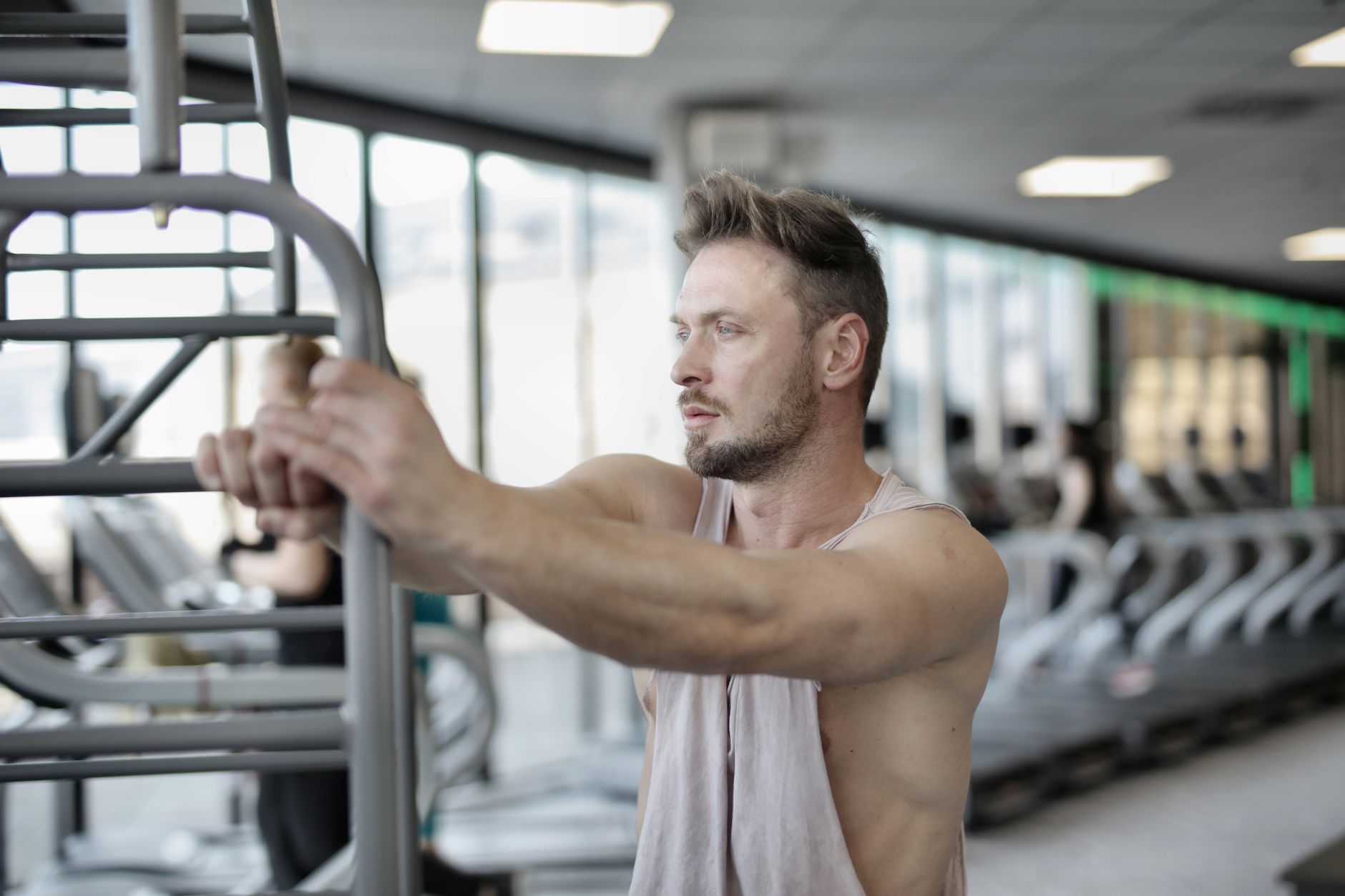 Serious young muscular sportsman in casual sportswear putting hands on metal railing while resting after intense workout in modern fitness center