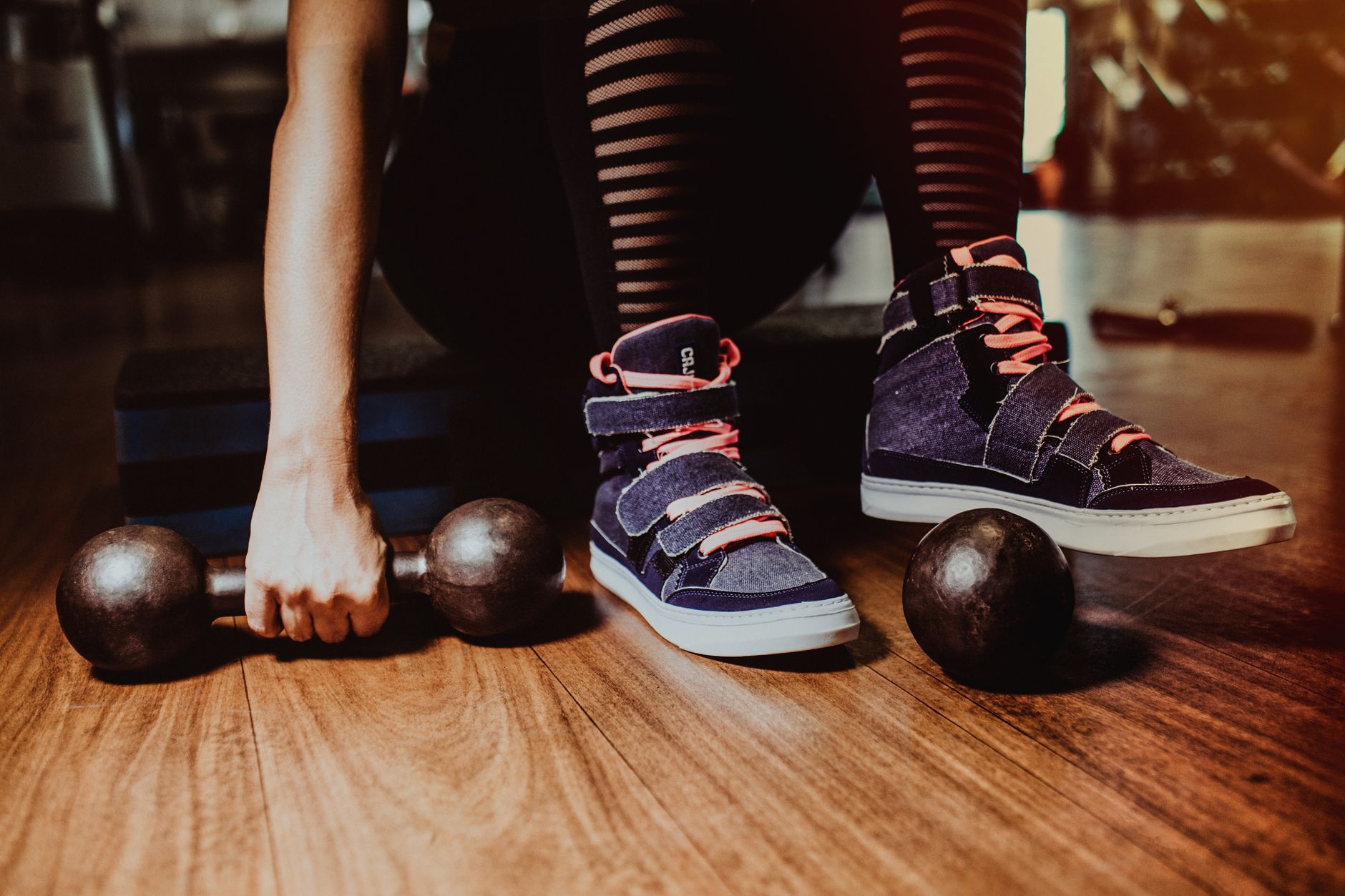 A person in striped leggings prepares for a workout with dumbbells indoors.