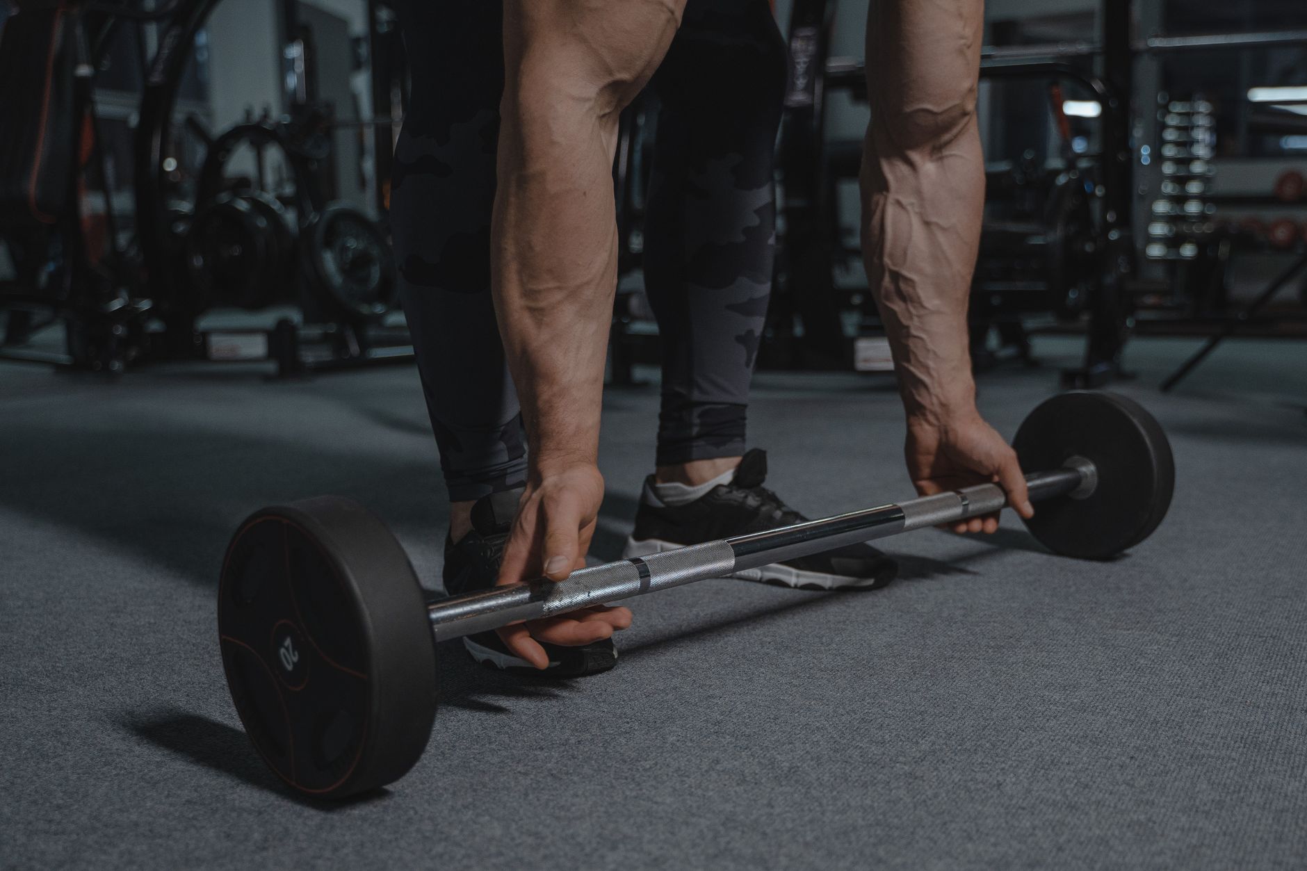 A muscular man grips a barbell in a dimly lit gym, preparing for a lift.