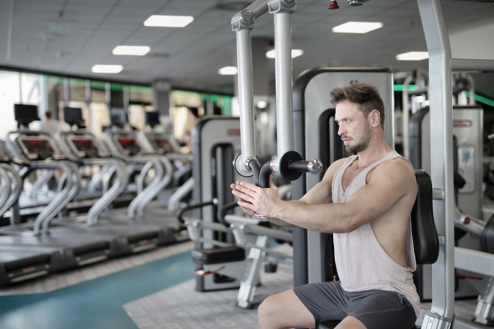 Serious strong male athlete in casual sportswear sitting on pec deck machine and performing exercise bringing hands together and looking forward in modern fitness center