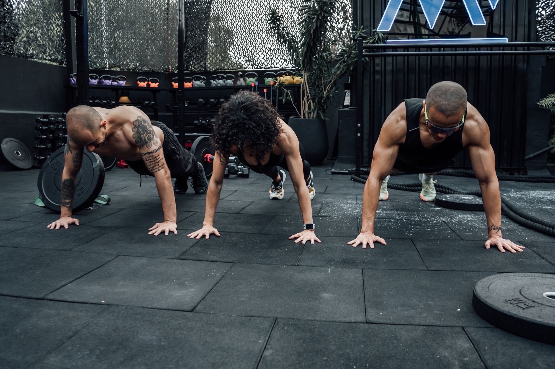 Three individuals performing push-ups together in a Mexico City gym setting.