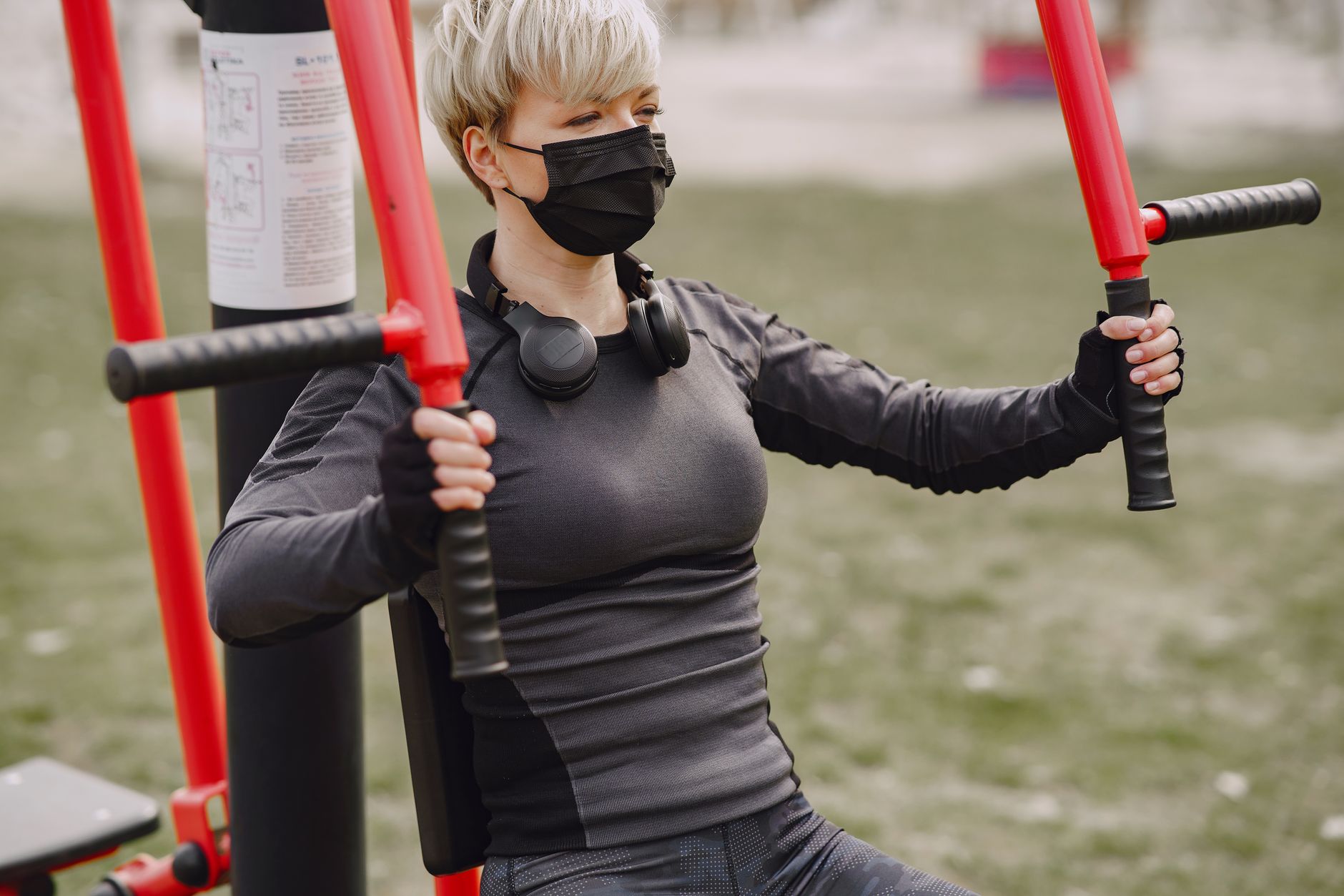 Strong crop sportswoman in sportswear and sport gloves wearing protective mask doing hands exercise on street workout equipment during quarantine in daytime
