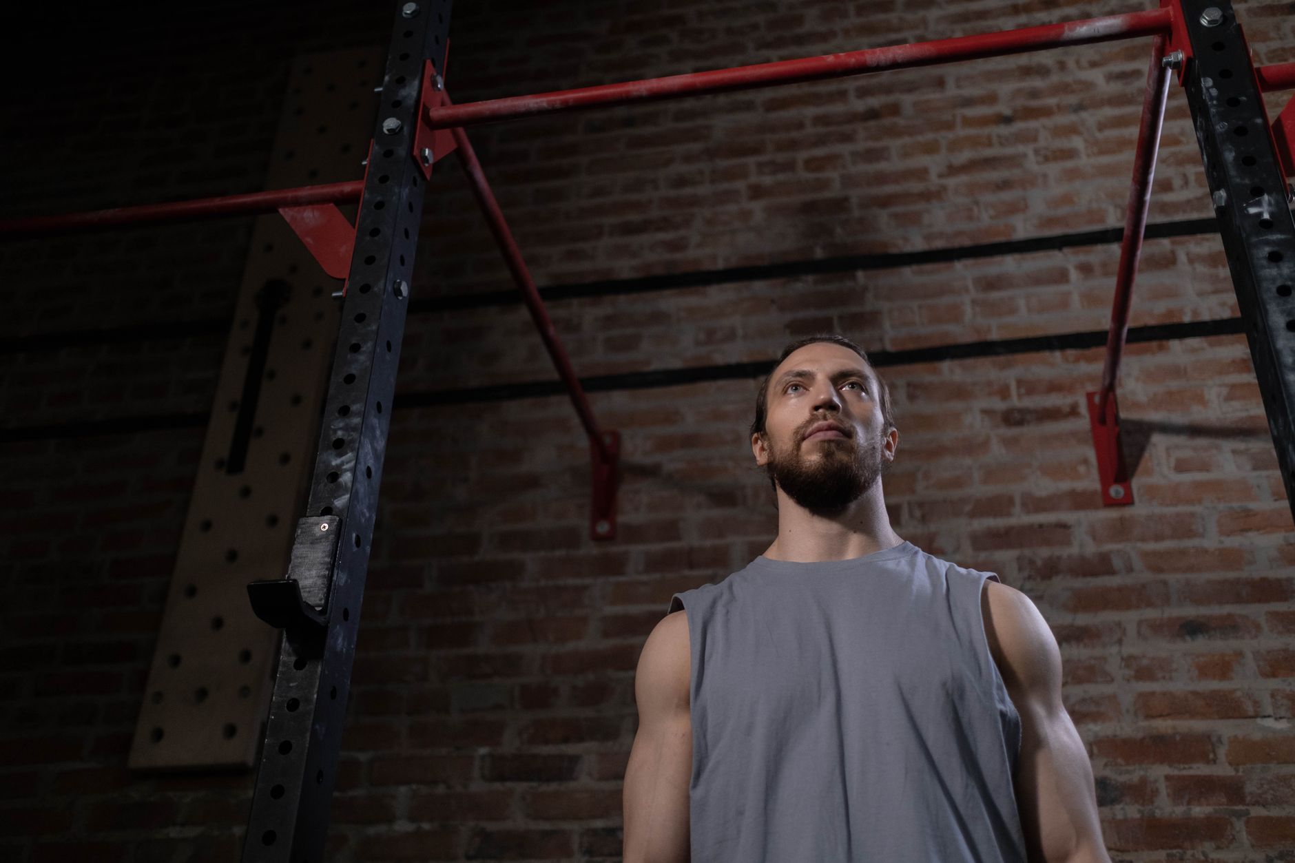 A strong, muscular man staring upward in a gym setting with brick walls.