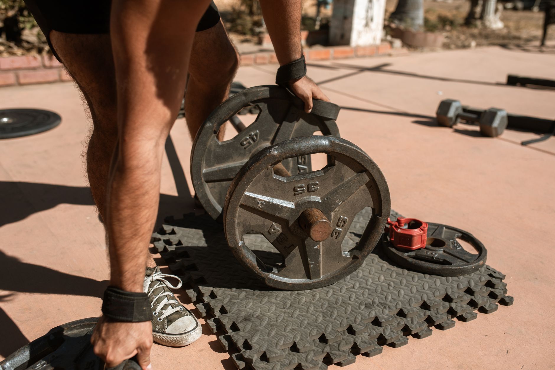 A man adjusts weight plates on a barbell during an outdoor workout session.