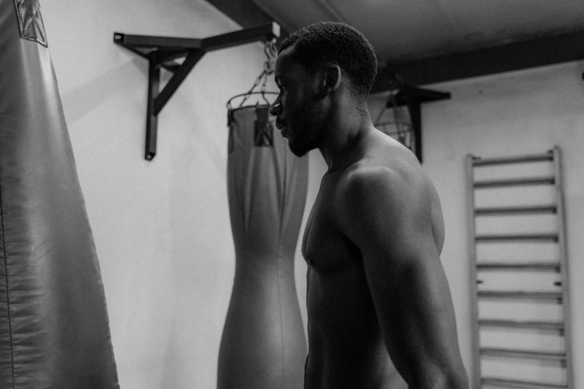 A muscular man in a gym focuses on training with punching bags in a monochrome setting.