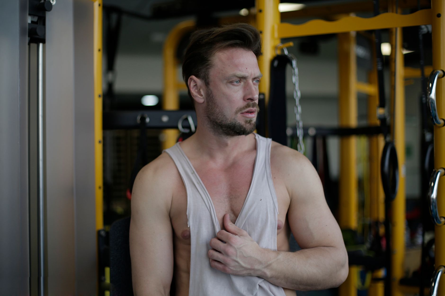 Powerful serious male athlete in sportswear standing in modern fitness center with sport equipment on background during workout and looking away pensively