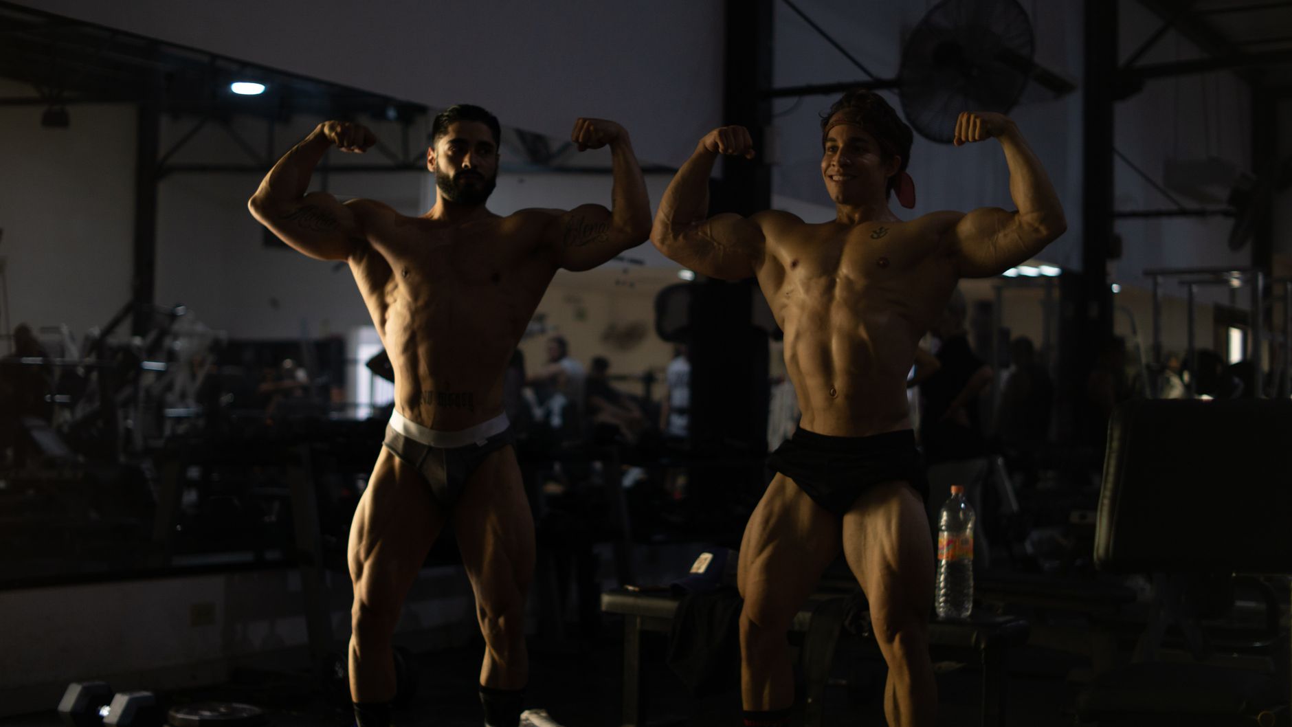 Bodybuilders posing and flexing their muscles in a gym setting, showcasing fitness and strength.