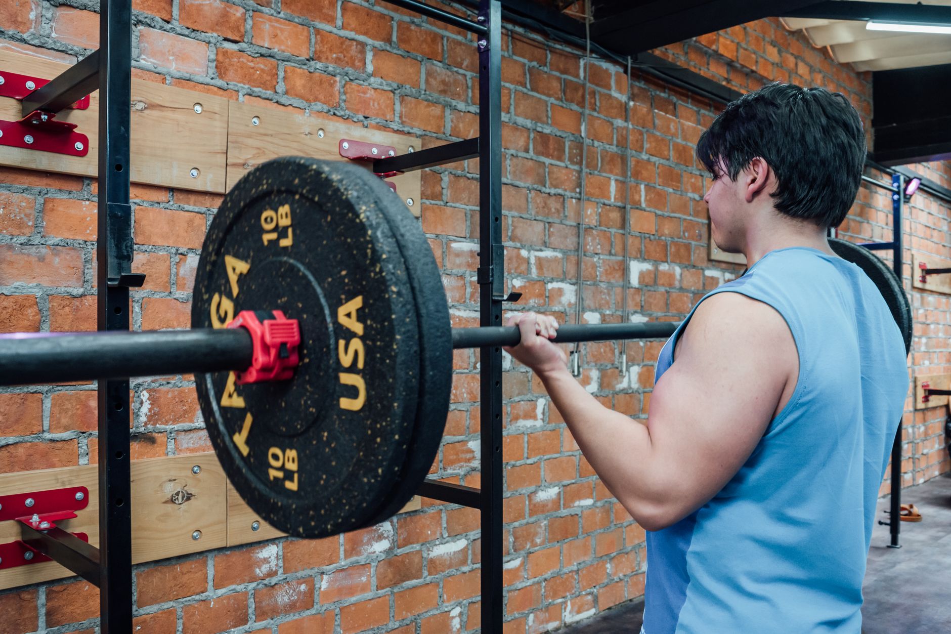 An adult male lifting weights on a barbell in a gym setting with brick walls in Mexico City.