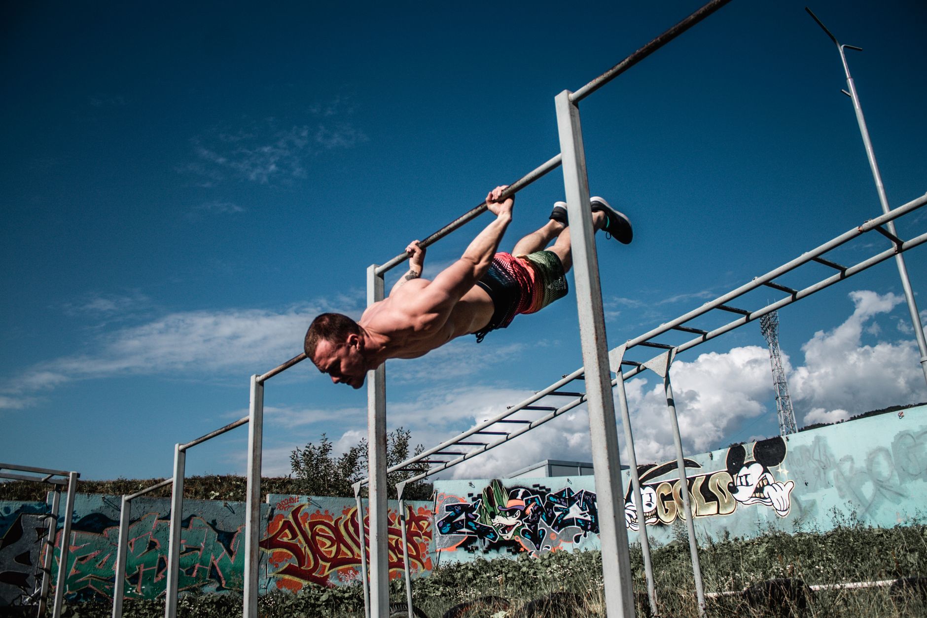 An athletic man doing a flag pose on outdoor gym bars with a graffiti wall backdrop.