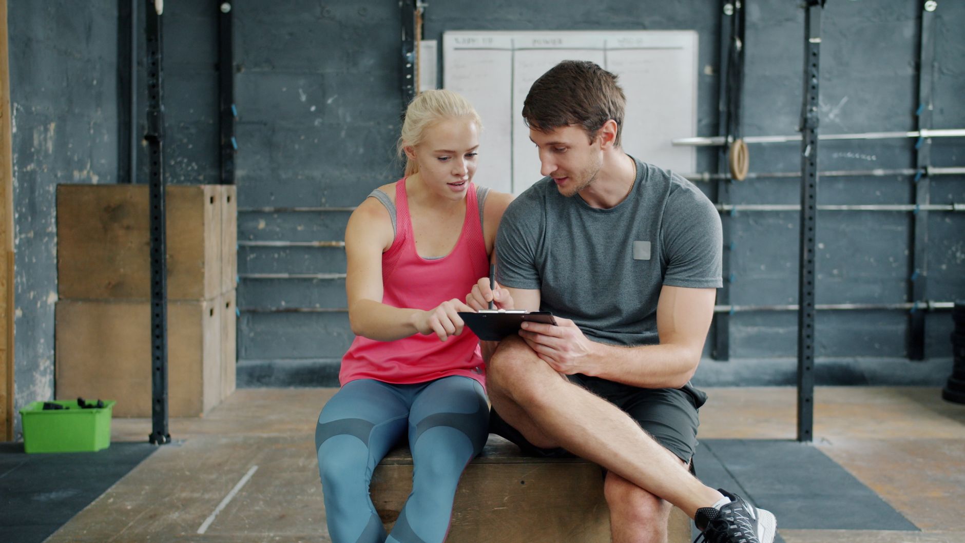 Man and woman in gym wear reviewing training plan on tablet indoors.