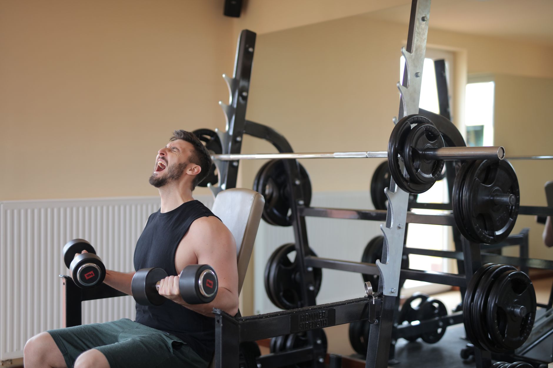 Man straining while lifting dumbbells in gym for strength training.