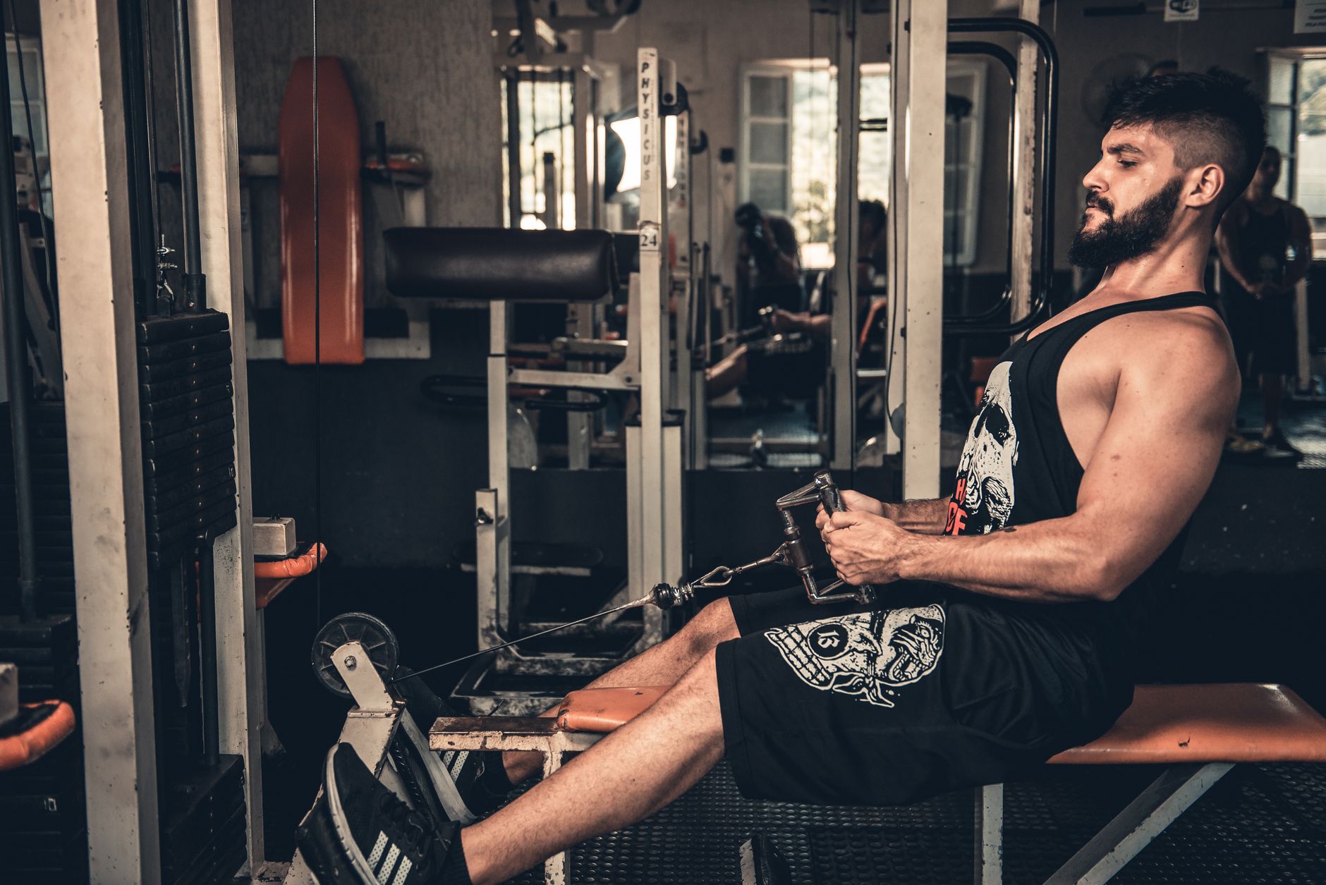 Muscular man focused on seated cable row training in an indoor gym setting.