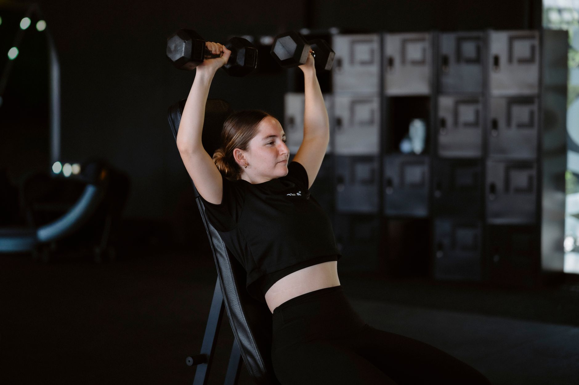 Young woman lifting dumbbells at gym showcasing strength training and fitness lifestyle.