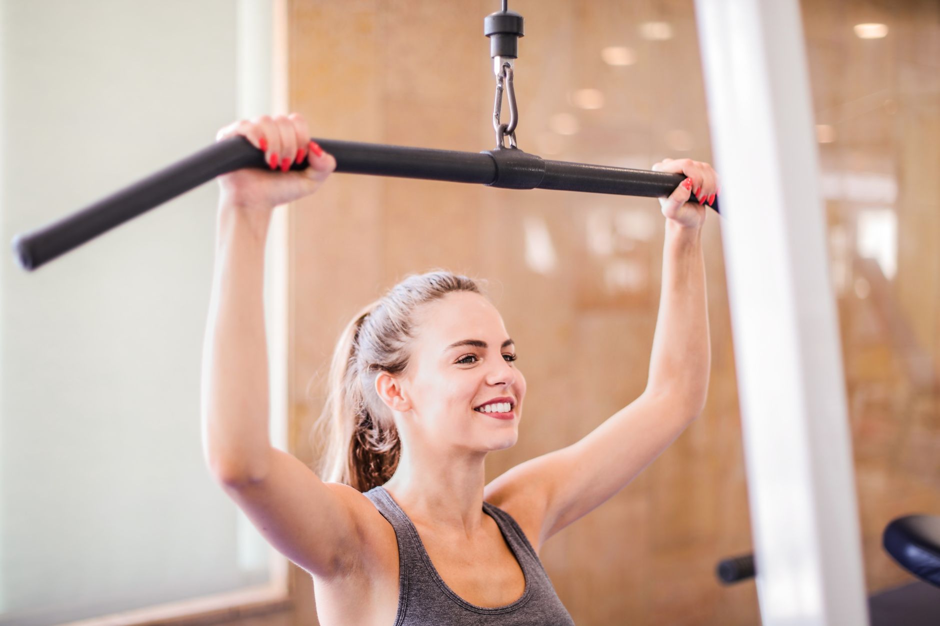 Smiling woman uses gym equipment for strength training indoors.