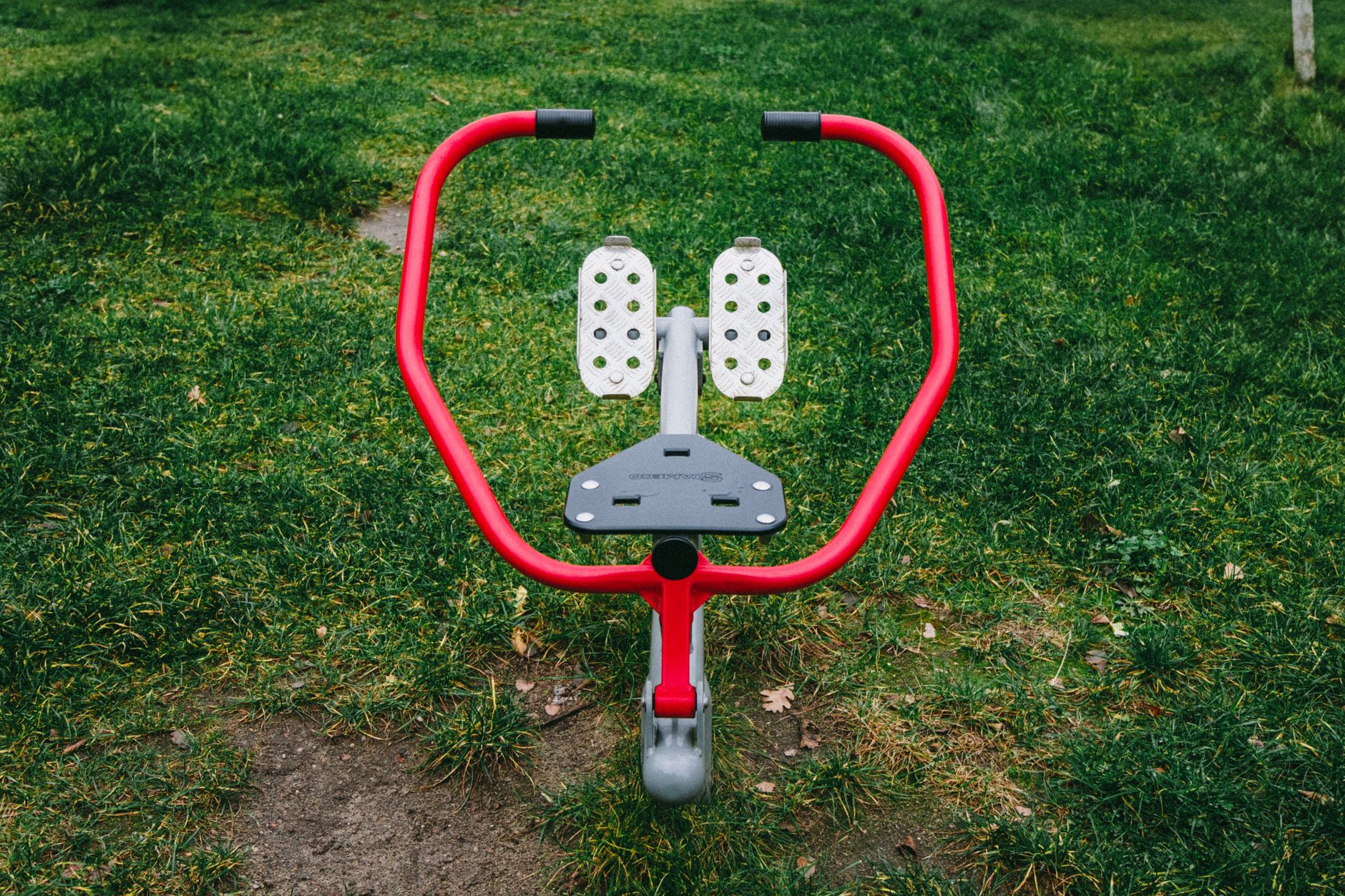 A vibrant red exercise device in a Polish park's green outdoor setting.
