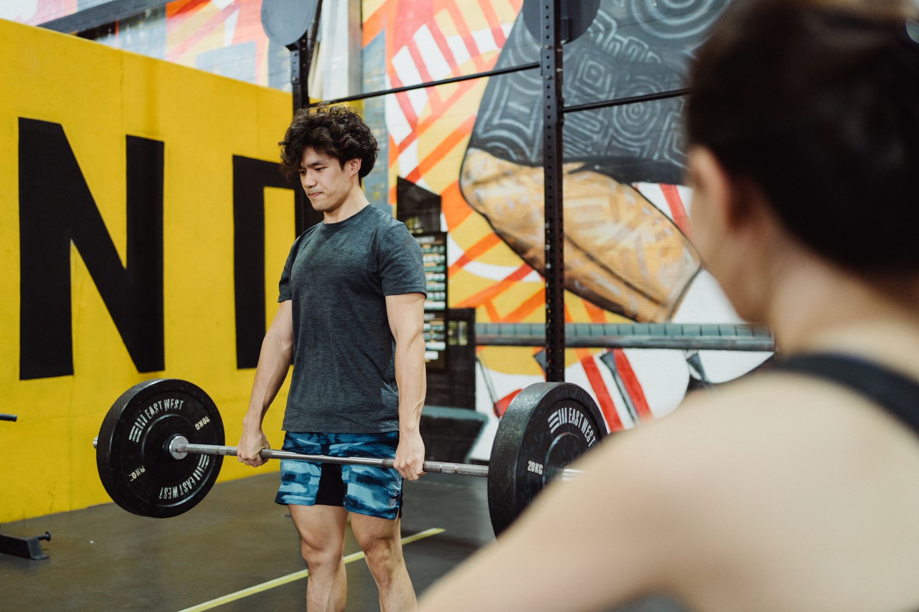 Muscular man lifting weights in an indoor gym with vibrant murals, embodying strength and focus.