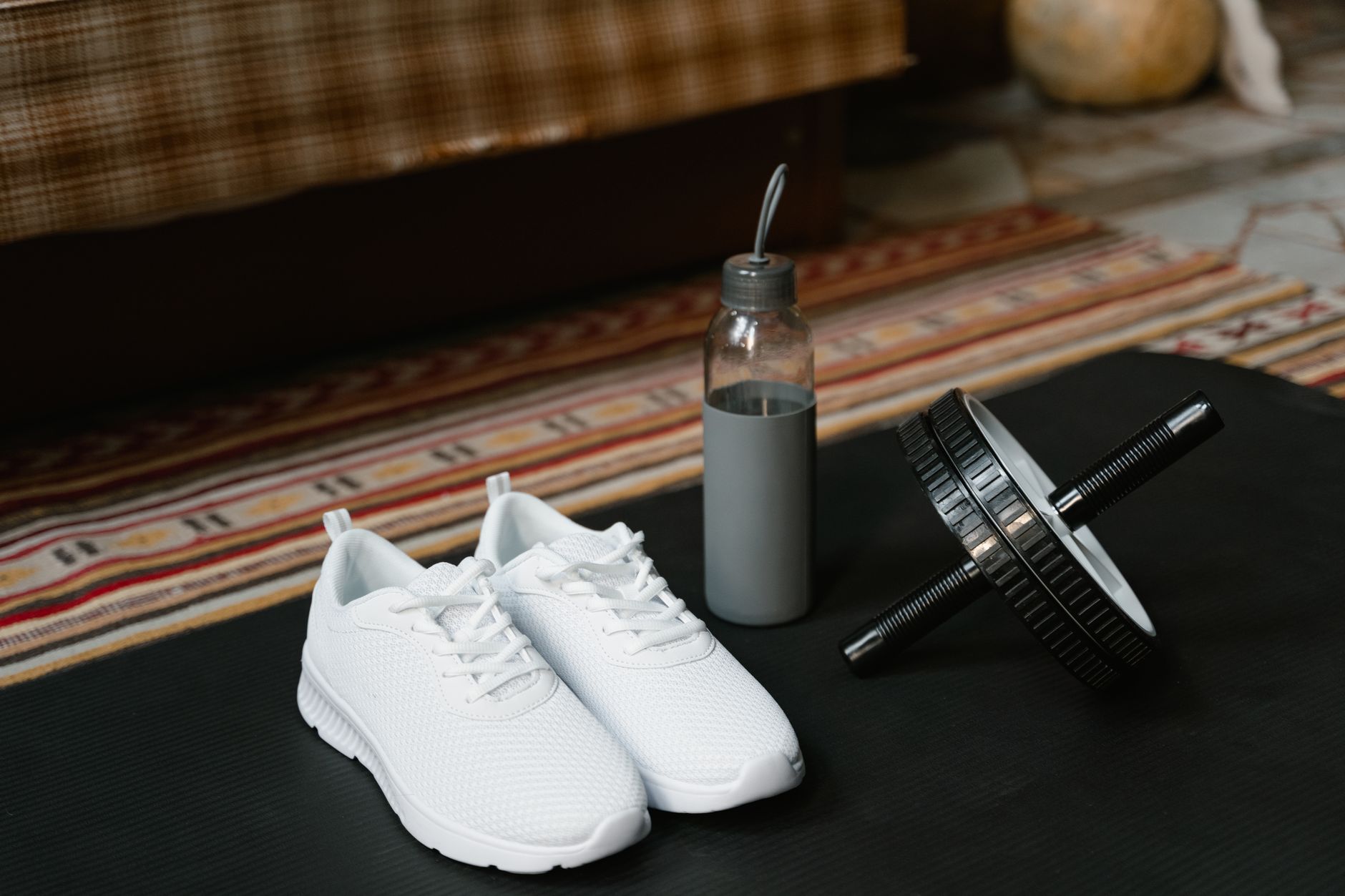 A set of fitness essentials including sneakers, an ab roller, and a water bottle indoors.