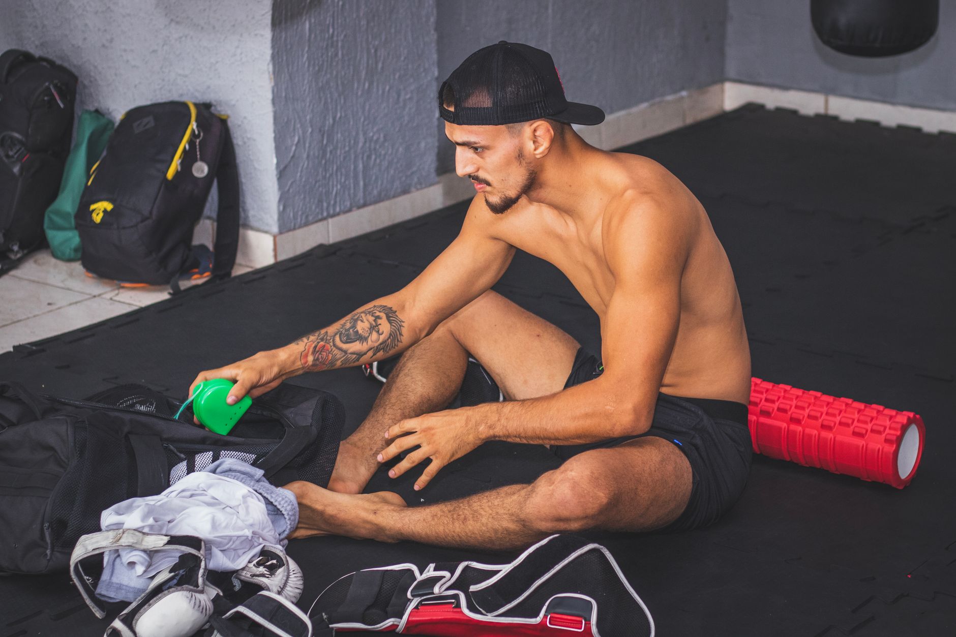 A fit young man with tattoos prepares for a workout, organizing his gym gear indoors.