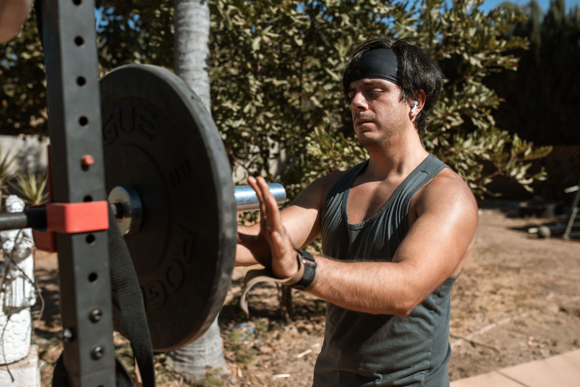 A young man adjusts a barbell in an outdoor gym setting, ready for a fitness workout.
