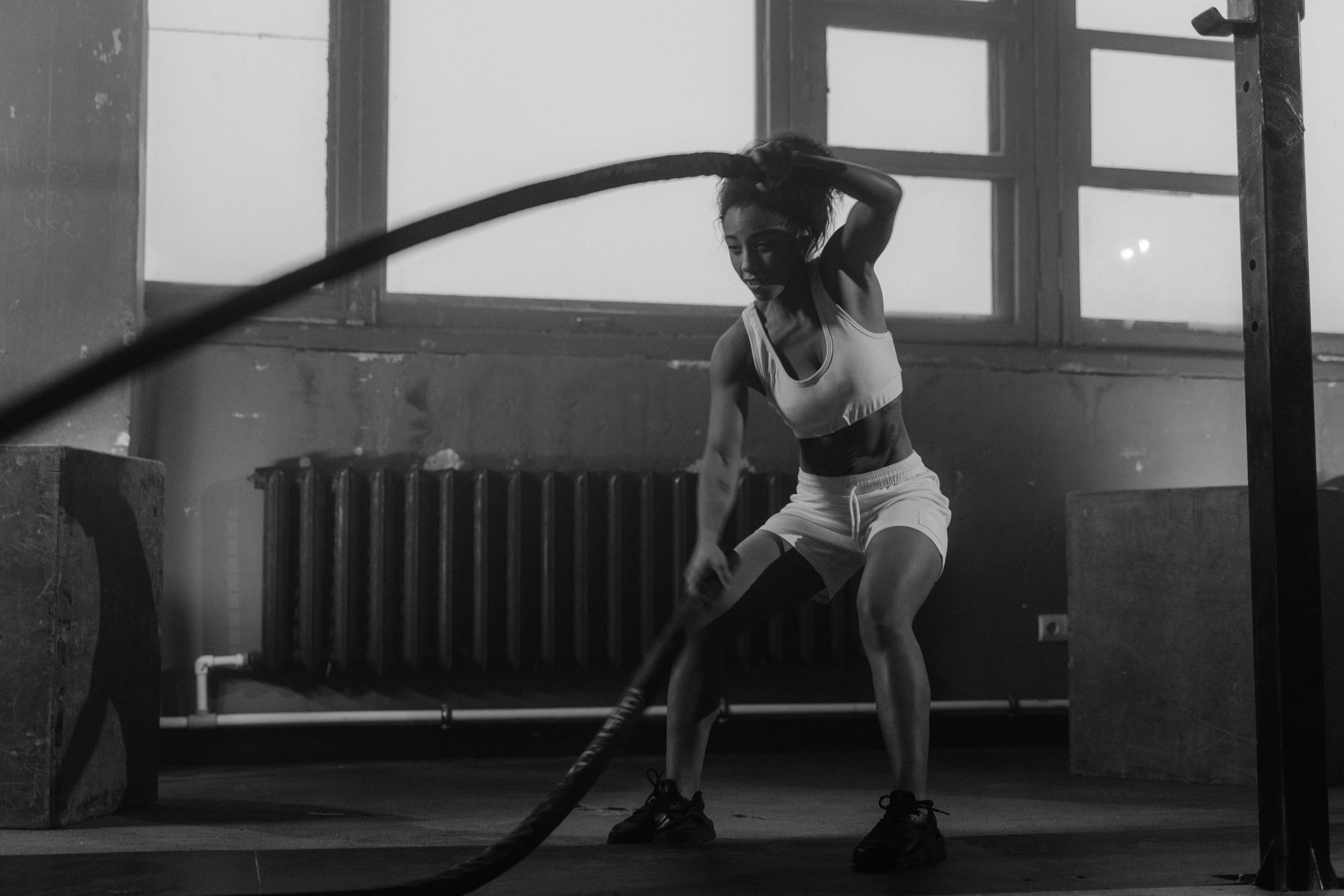 Woman in a gym engaging in vigorous battle rope workout for fitness.