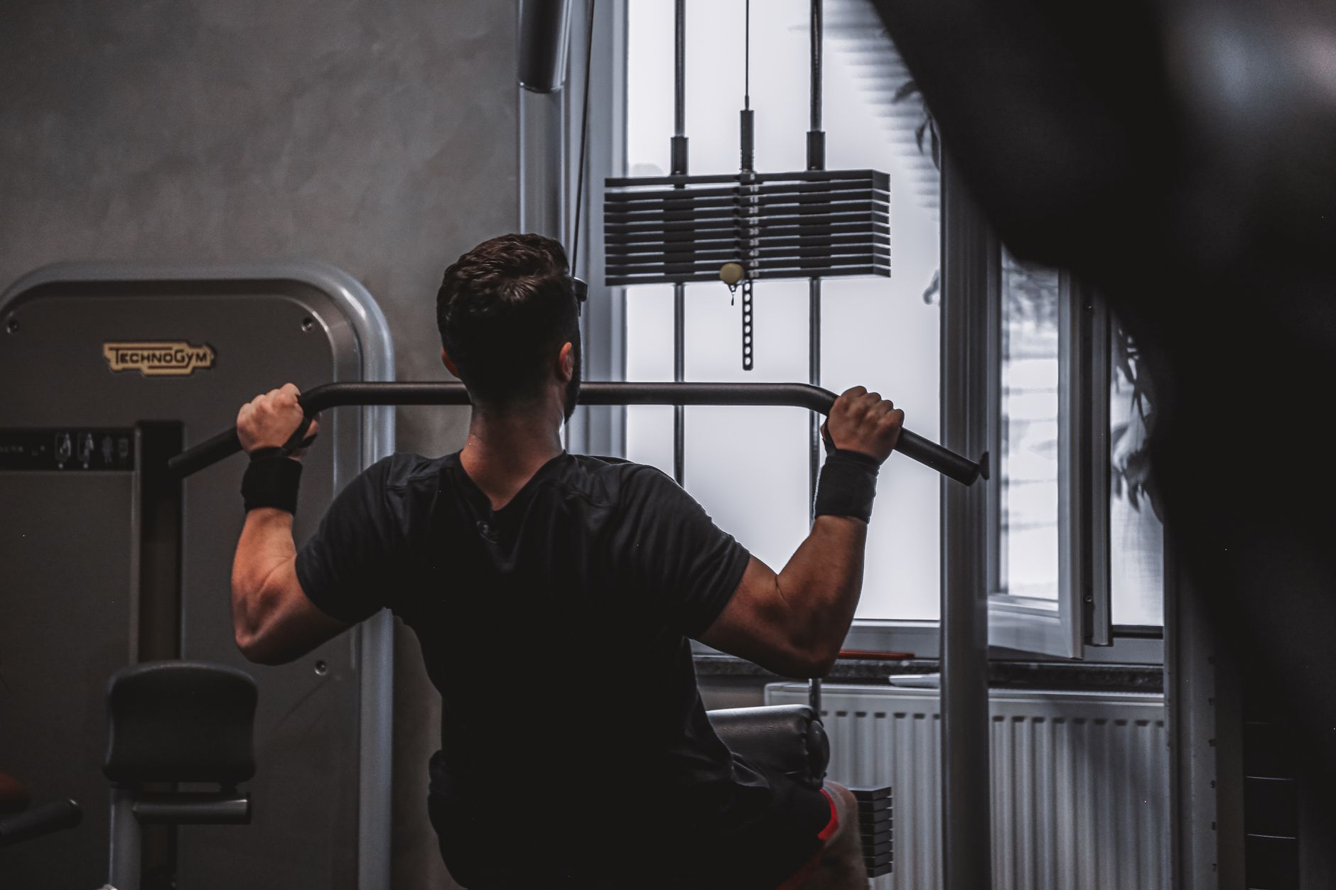 Back view of a man exercising with lat pulldown machine in the gym.