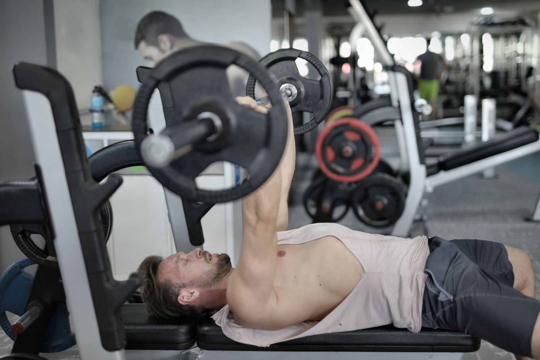 Side view of strong young sportsman in  sportswear lying on bench and pressing heavy barbell doing chest exercise training in modern gym