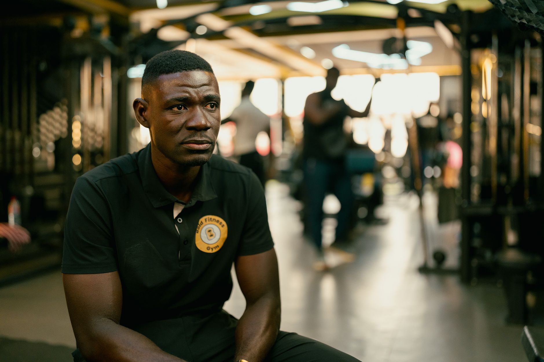 Gym trainer sitting in a modern fitness center with blurred background. Calm and focused expression.