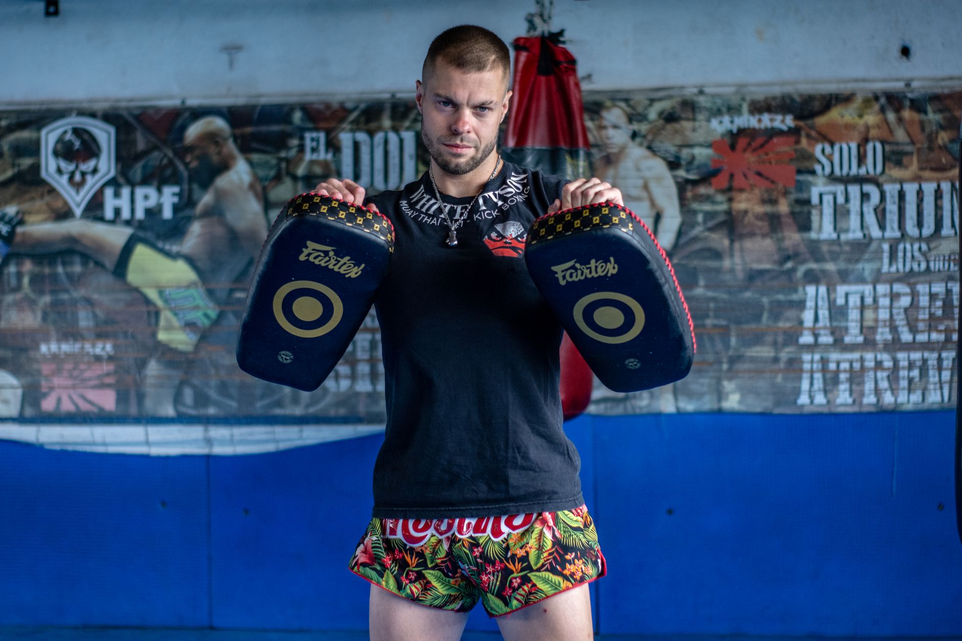 A male kickboxing trainer posing with focus pads in a gym, showcasing martial arts discipline.