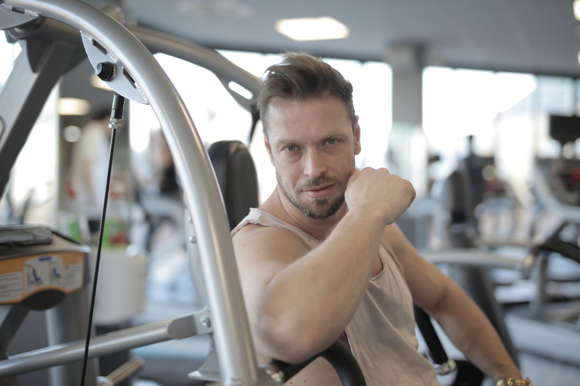 Muscular sportsman having break after hard training in modern gym while sitting and looking at camera