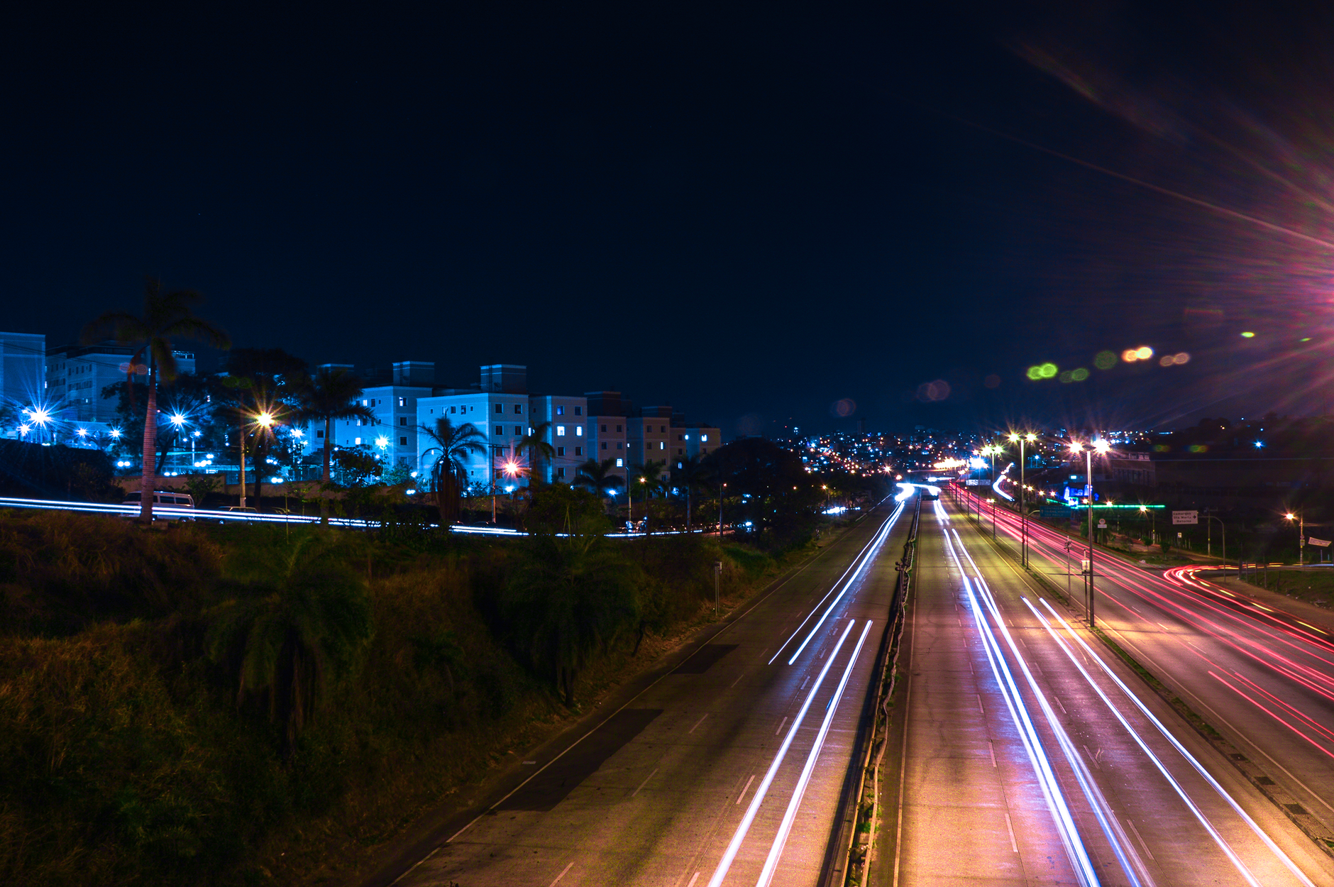 A dynamic night view of a city highway with vibrant light trails and illuminated buildings.