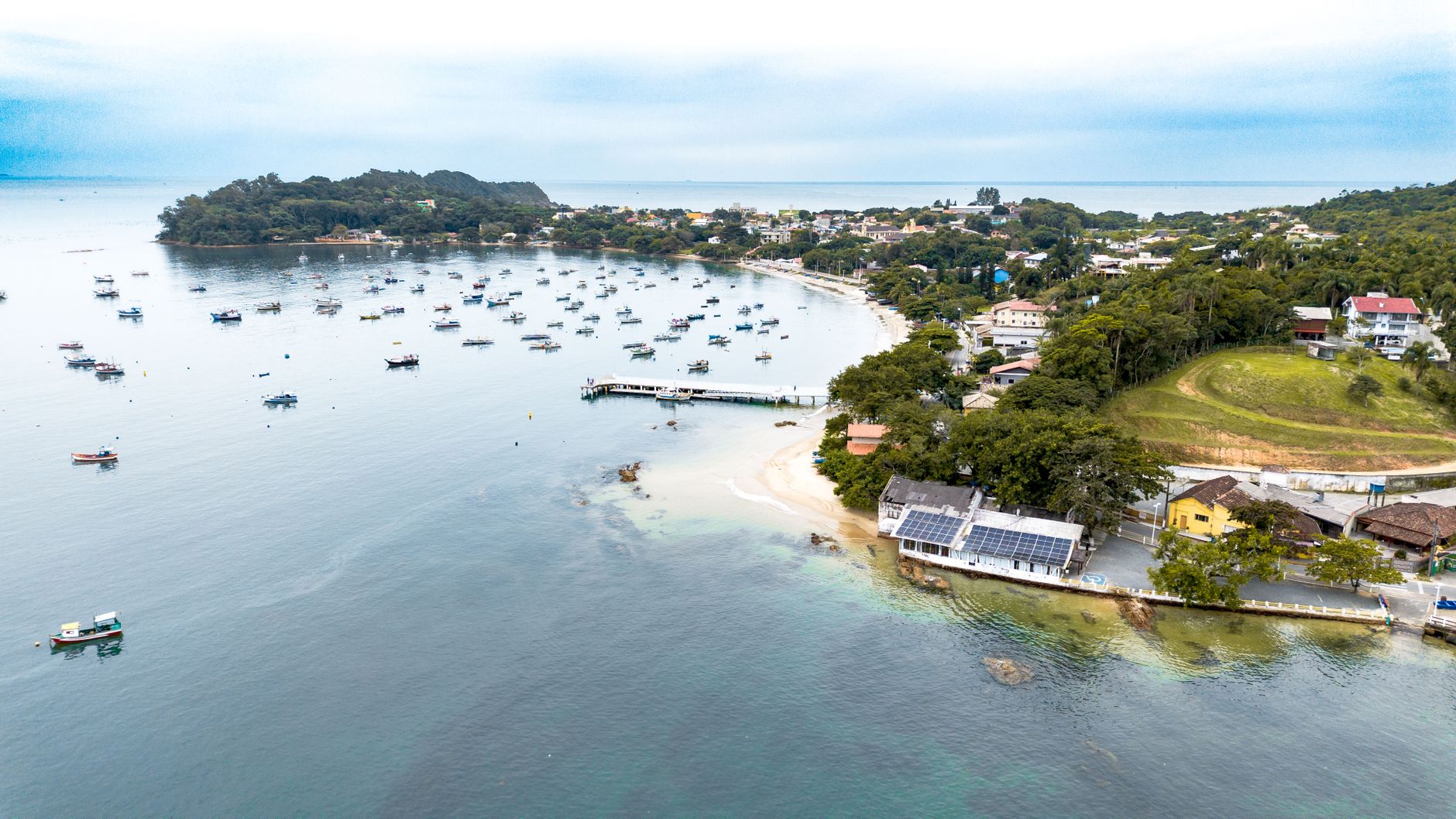 Aerial view of a coastal town with a busy harbor, showcasing numerous boats and lush greenery.