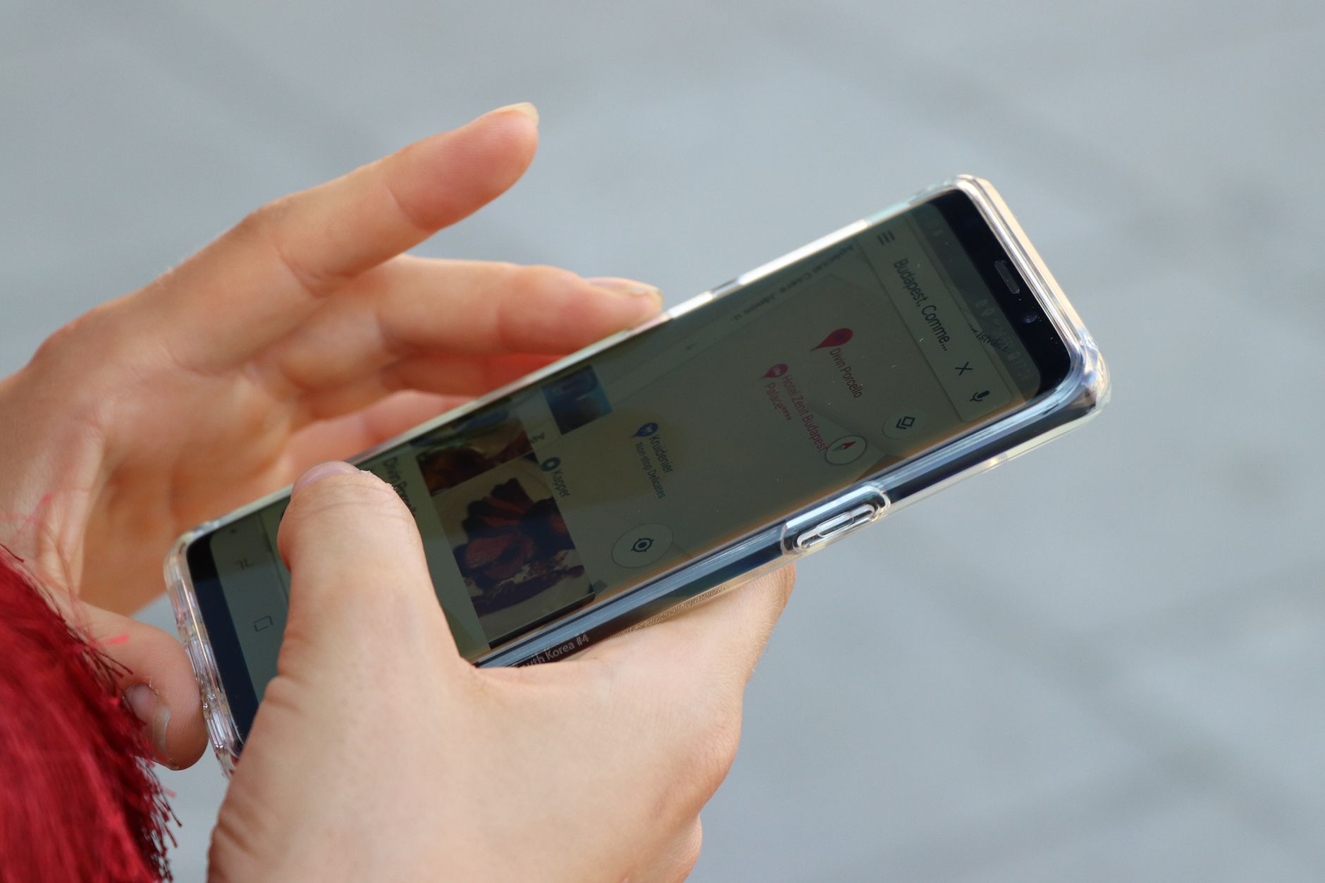 Hands holding a smartphone with a clear case, browsing a map outdoors.