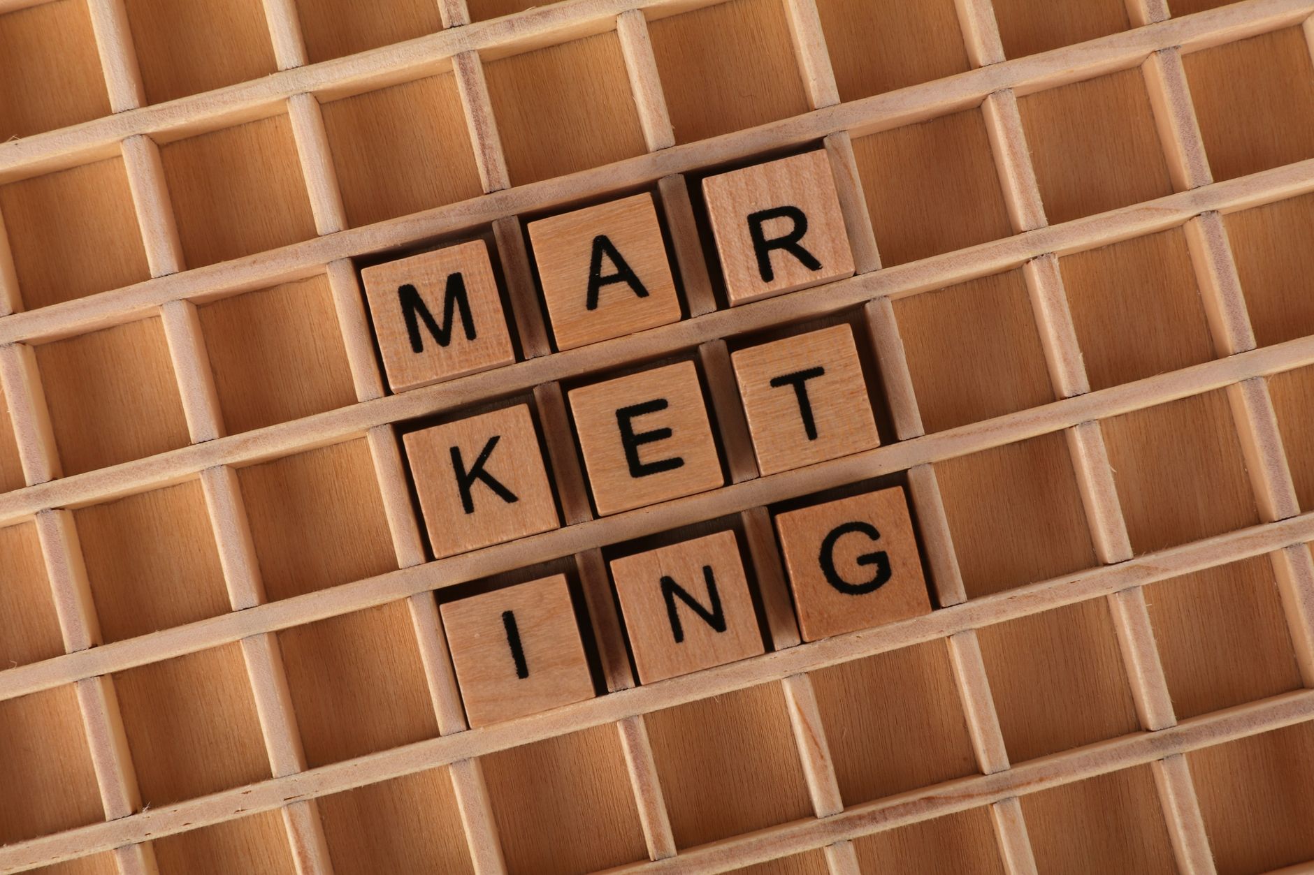 Wooden letter tiles spelling 'Marketing' on a wooden grid, emphasizing strategy and planning concepts.