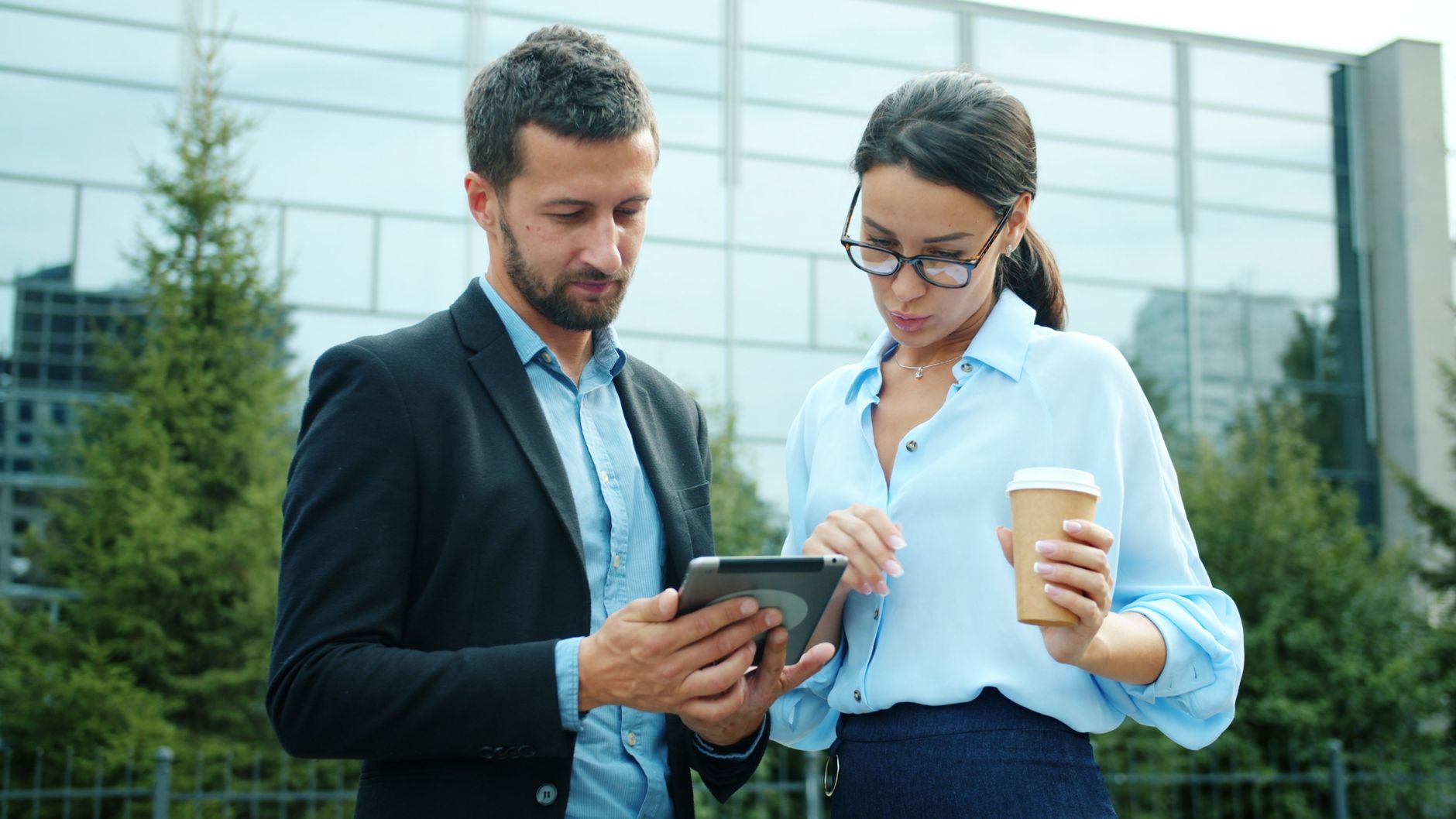 Two business professionals reviewing content on a tablet outside an office building.