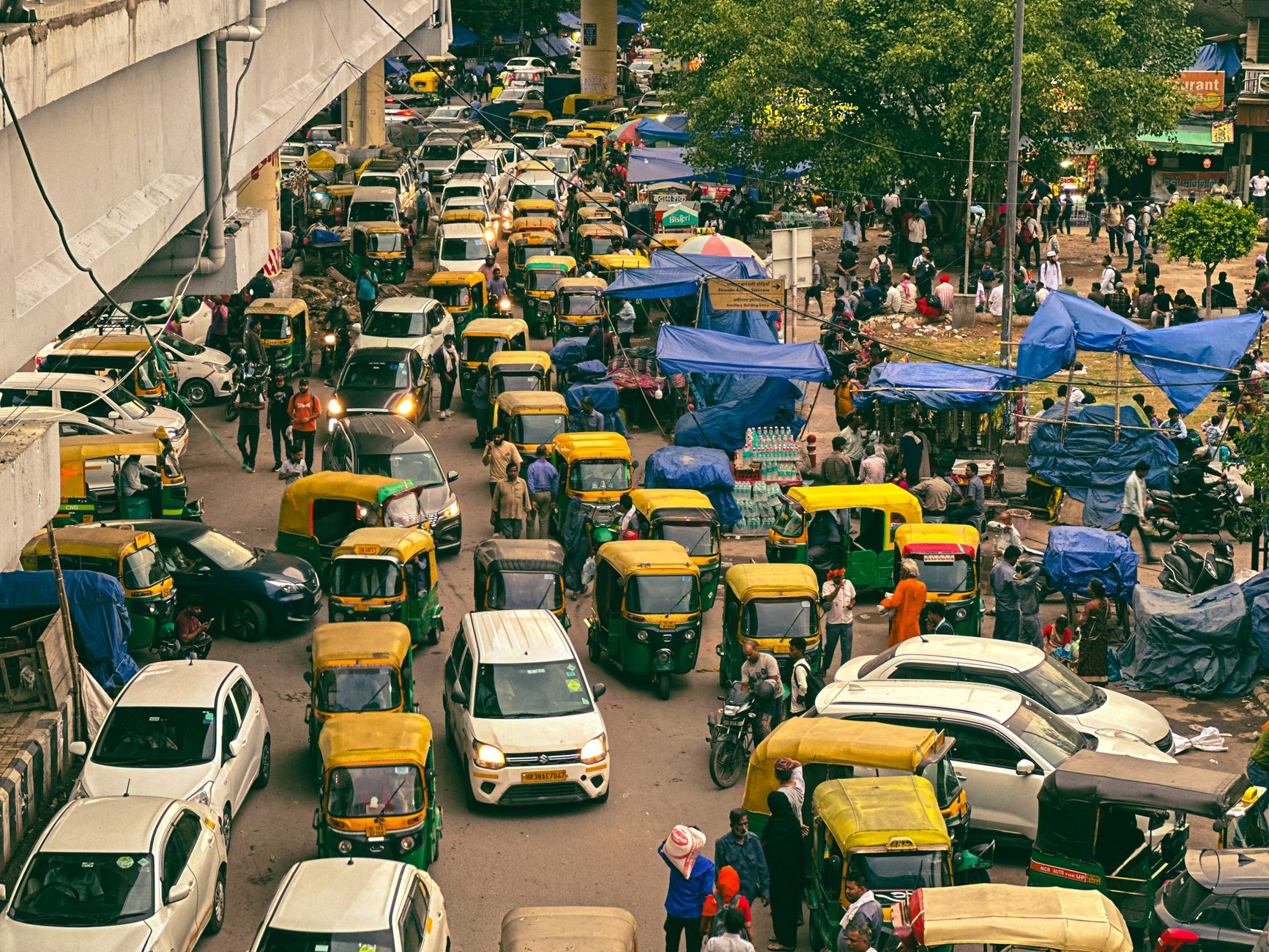 Dynamic aerial view of a busy New Delhi street with auto-rickshaws and pedestrians in a lively market.